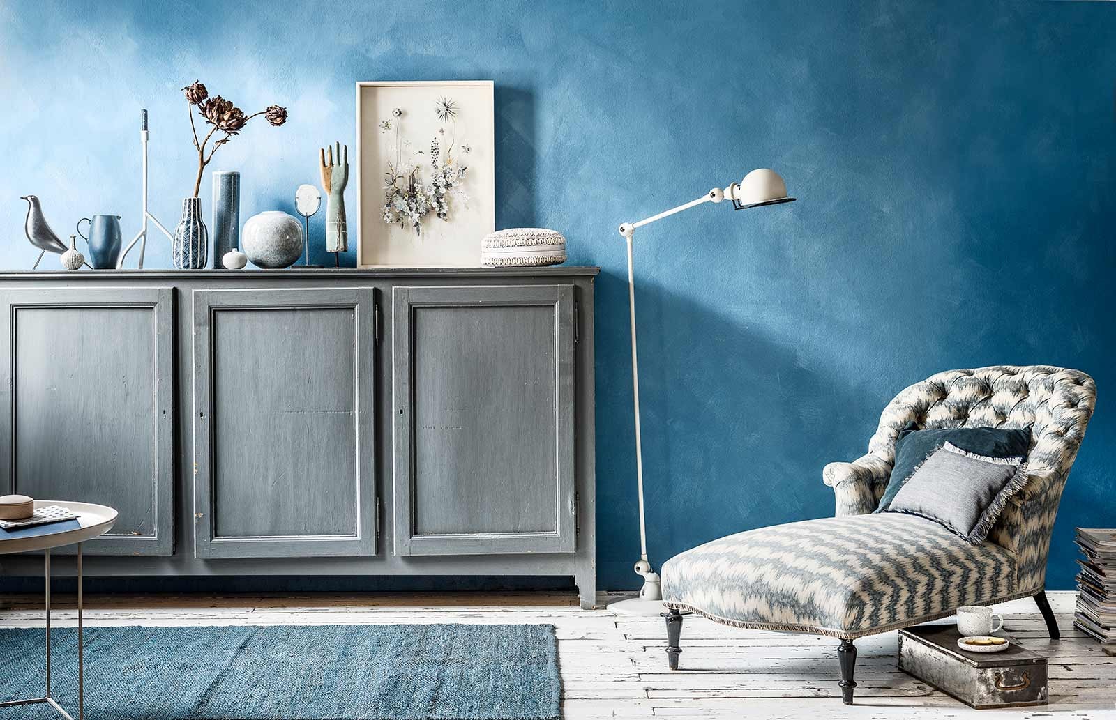 Muurverf in kleur Periwinkle van Bauwerk Color (). Lichtgrijze bijzettafel (). Schrift met blauwe stippen, schaaltje van esdoornhout met deksel, grijs kussen met blauw-witte rafels (). Blauw vloerkleed, blauw fluwelen kussen, metalen kluiskistje, waxinelichthouder op pootje met agaat, houten hand op pootje (). Grijs houten dressoir (). Zwarte vogel van Eames (). Minivaasjes van keramiek (). Blauwe kan, blauw-wit gestreepte vaas, antieke chaise longue met originele bekleding (). Kandelaar op pootjes (). Gedroogde artisjokken (). Langwerpige vaas (). Gevlekte ronde vaas (). Kunstwerk Flower Construction 88 gemaakt van droogbloemen en papier (). Ronde schelpenmand (). Witte Jieldé lamp in kleur Elephant Breath van Farrow &amp; Ball prijs op aanvraag (). Witte mok met zwarte vlekjes, witte schotel met zwarte vlekjes (). Overig privébezit.
