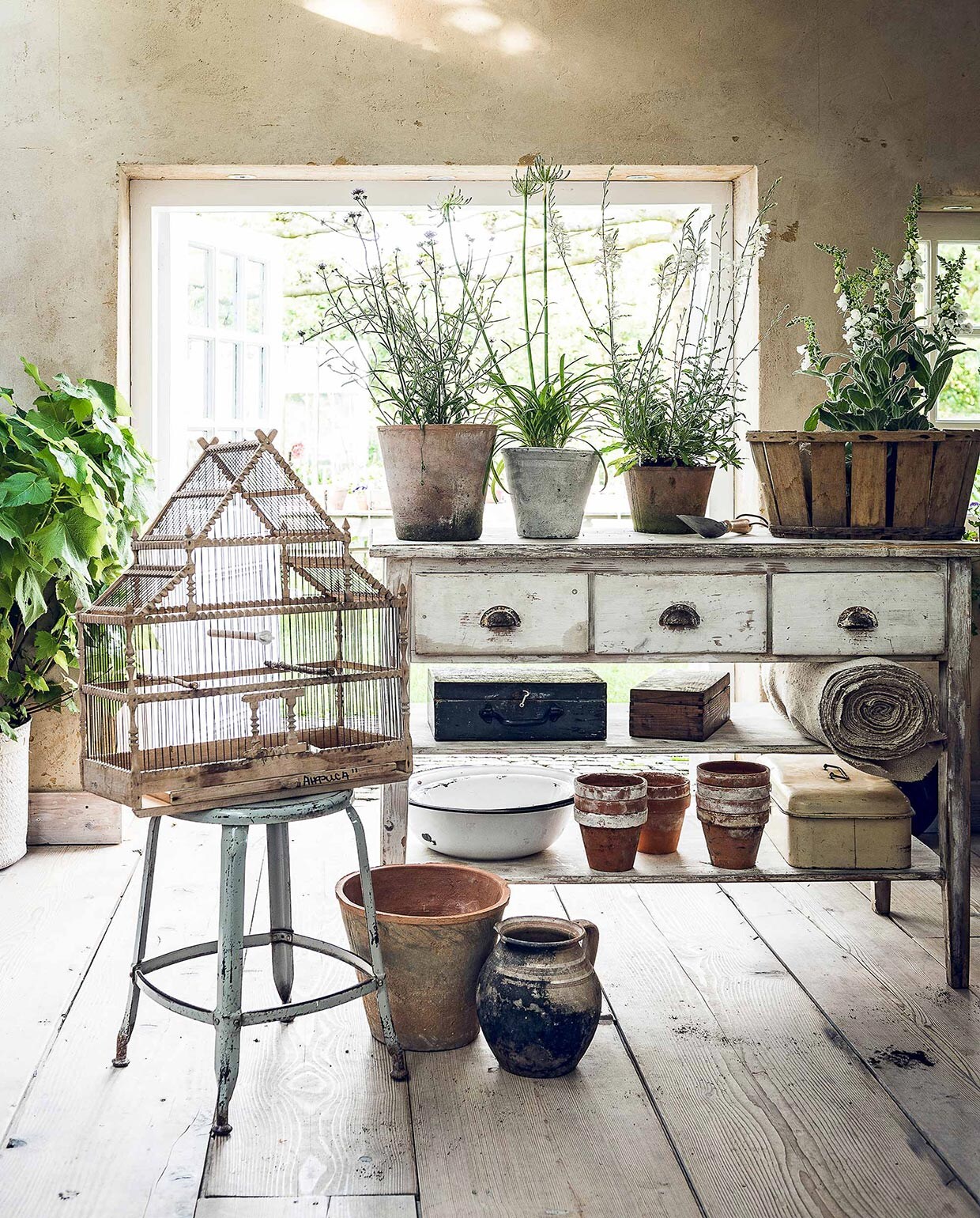 Metalen kruk (). Vogelkooi, oud linnen op rol, oude broodtrommel (). Werktafel, emaillen teilen, houten kisten (). Terracotta bloempotten (). Witte bloempot, houten mand (). Handschep (). Overig privébezit., vtwonen 07-2017 | Fotografie Sjoerd Eickmans | Styling Danielle Verheul