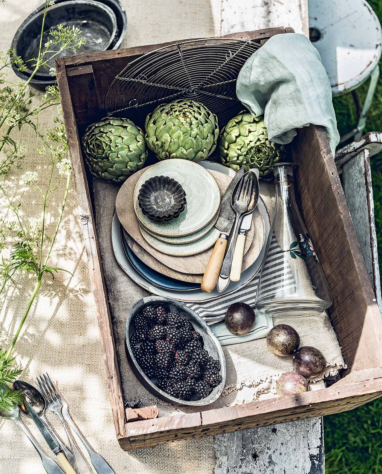 Oud linnen op rol, oude houten kist, opgevouwen tafelkleed van canvas (). Metalen schaaltjes, wit bord met ‘oud’ randje, zwart-wit gestreepte tafelloper, groene servetten, witte klapstoel (). Zachtgroene gebaksbordjes (). Mangohouten borden (). Karaf met bloemprint (). Witte metalen kruk (). Overig privébezit. vtwonen 07-2017 | Fotografie Sjoerd Eickmans | Styling Danielle Verheul