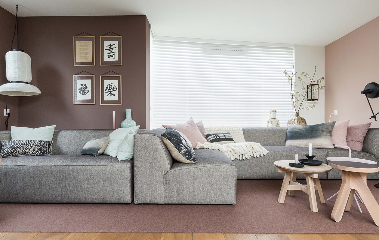 Houten jaloezieën: . Kleur op de wand – Karton S3010-Y70R: . Bank: . Kussens – mint: . Kussen – grafisch: . Kussen – gevlekt: . Kussen – bomen: . Kussens – roze: . Kussen – crème zwart: . Plaid: . Kussen – gevlekt: . Buddha: privébezit. Vaas: . Display box: . Fotolijsten: privébezit. Vloerlamp: . Springbok: . Vloerkleed:  (verkrijgbaar in de winkel). Salontafel – roze: . Kruk – donkerhout: . Salontafel – lichthout: . Kandelaar – zwart:. Plafondlamp: vtwonen weer verliefd op je huis |  seizoen 6 aflevering 7 | Styling Marianne Luning | Fotografie Barbara Kieboom