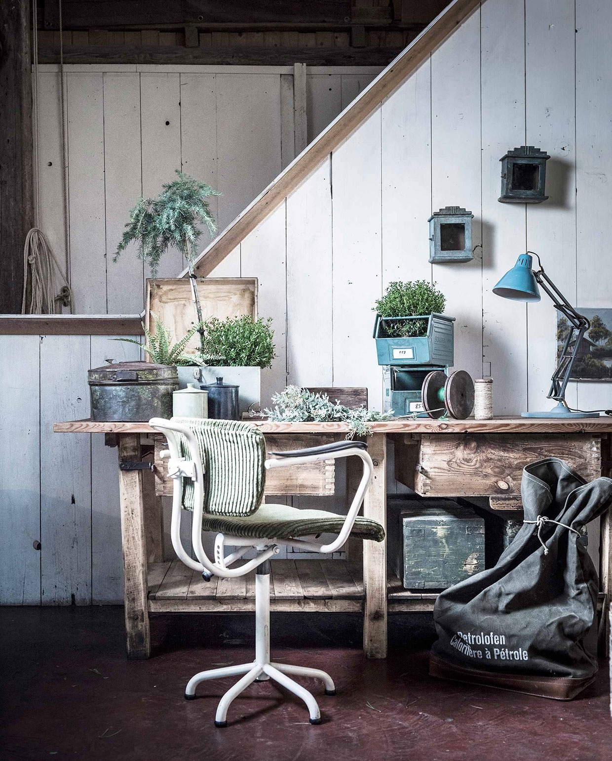 Houten werkbank, mintgroene kist, schilderij, legerkisten (). Bureaustoel, bureaulamp (). Ovale stalen kist, kastjes aan de muur (). Zwarte pot, witte pot (). Stalen opbergbakken, garenhouder met groen garen (). Klos met wit touw (). Groene legertas ()., vtwonen 03-2017 | Fotografie Sjoerd Eickmans | Styling Liza Wassenaar
