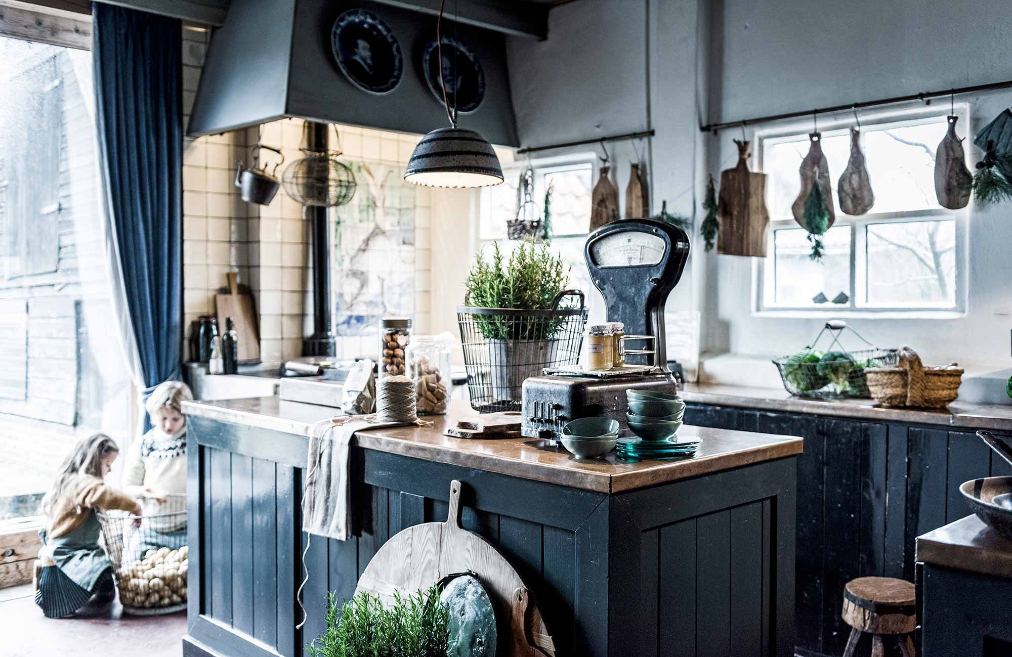 Ovale stalen mand prijs op aanvraag (). Stalen mand, snijblok, broodplanken (). Zwarte weegschaal (). Theedoek (). Groene schaaltjes, groene borden van glas, meel voor pasta, jam (). Bruine mand voor eitjes, glazen pot met walnoten (). Klein hakblok, koekjespot (). Groen schort (). Gele trui, groene jurk, gebreide trui met print (). Theepot (kringloopwinkel). Overig privébezit., vtwonen 03-2017 | Fotografie Sjoerd Eickmans | Styling Liza Wassenaar