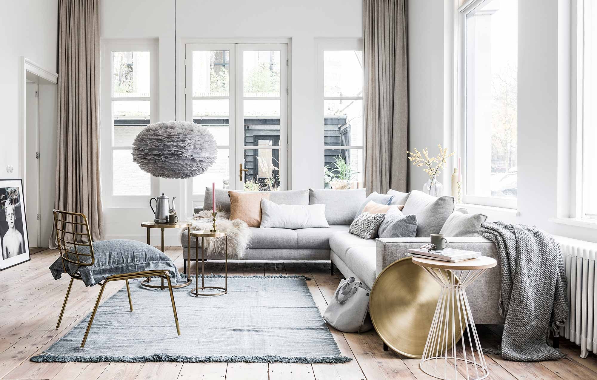 Hoekbank Aikon Lounge van Design on Stock, wit draadwerk tafeltje (). Schapenvacht krul (). Linnen  in zachte pastellen van By Mölle, goudkleurige draadwerk  Mesh van Bloomingville (). Blauw fluwelen kussen (). Grijs kussentje met lusjes, grijze tas van Zusss (). Grijze deken met gerstekorreldessin, kandelaar groot, kandelaar (). Brass tafeltjes Alex per set van 2, blauw chambray kussen van vtwonen, goudkleurig dienblad Brass (). Vloerkleed Mekong Nights Stonewash Blue L (). Hanglamp Eos van grijze veertjes, kopjes per stuk (). Lijst met foto van kind gemaakt door fotografe Linelle Deunk. Koffiekan en glazen vaas privébezit.