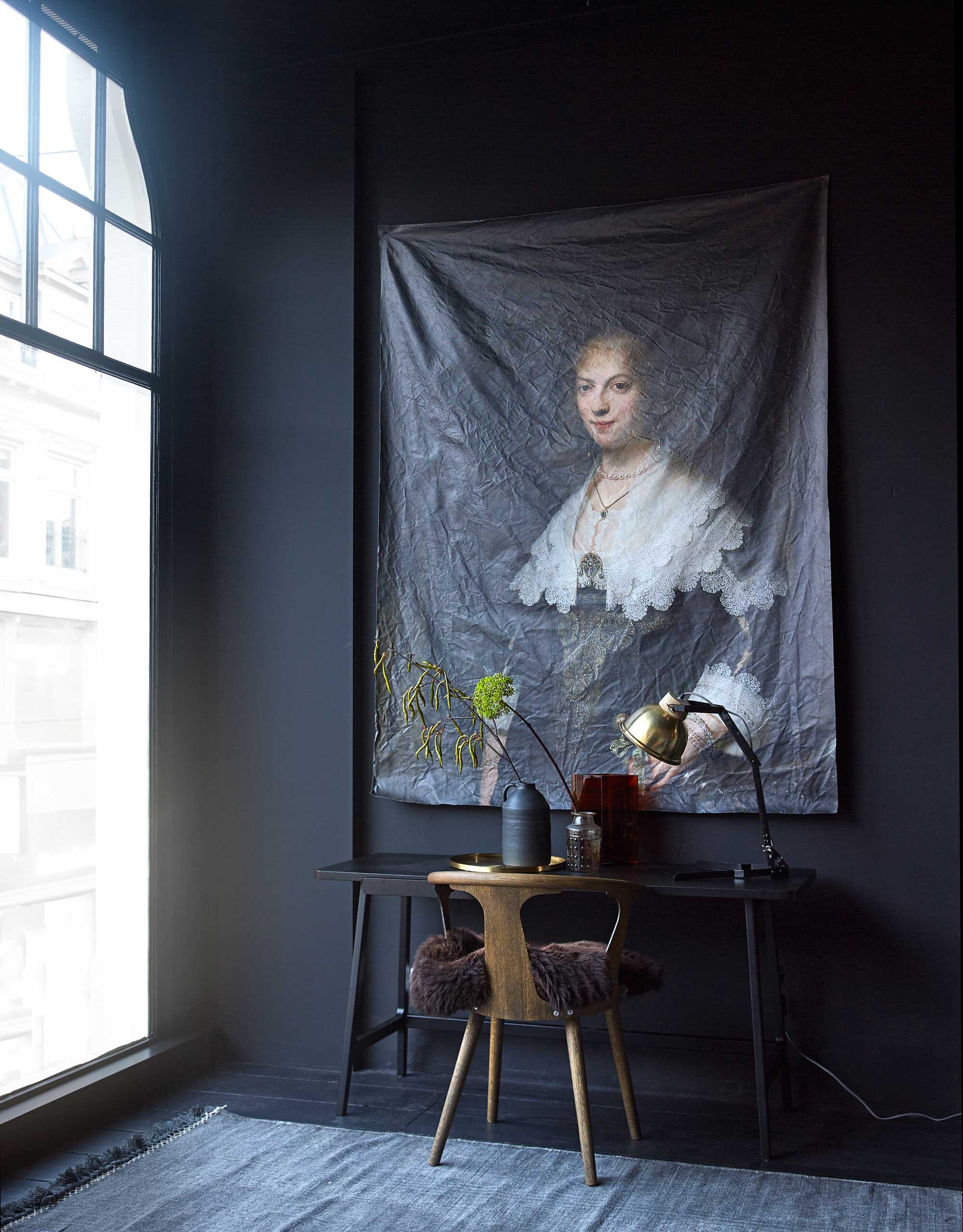 Muurverf Off Black uit de vtwonen verfcollectie (Karwei). Groot canvas doek met afdruk van schilderij van Rembrandt van Rijn, 145×190 cm (More than Canvas). Bureau van Arflex, 140x50x71 cm (lxbxh), stoel van &amp;Tradition (Mobilia). Vaas met mat glazuur , goudkleurig dienblad, vachtje (Nijhof). Glazen vaasje van Madam Stoltz, lamp van Madam Stoltz (deens.nl). Glazen vaas Cranberry van Iittala (Mobilia). Vloerkleed 140×200 cm (Aai Made with Love).