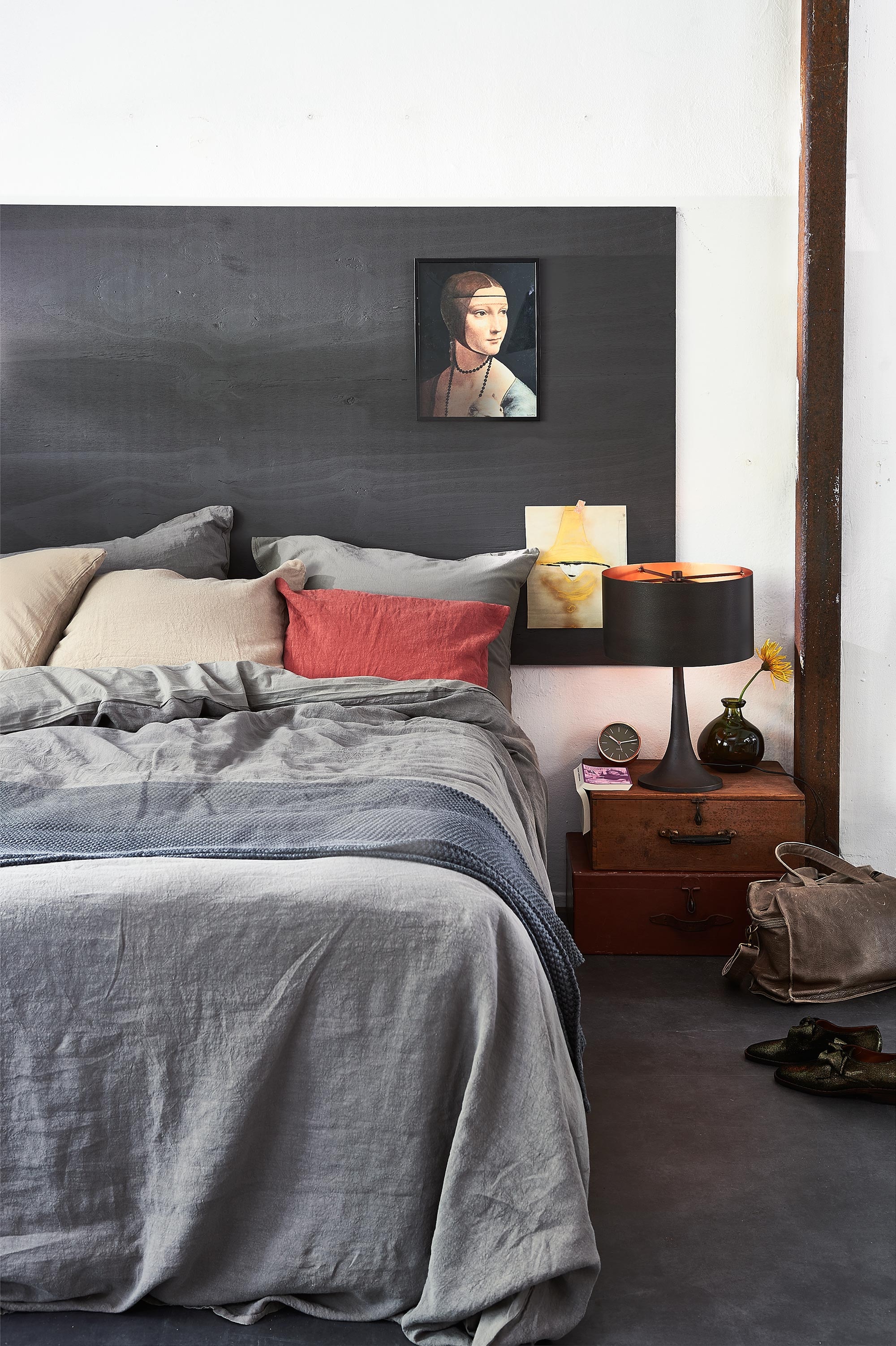 Linnen beddengoed, kussensloop, plaid, rood kussenhoesje (Vandyck). Aan de wand poster Mary (Raw Materials). Kisten naast bed (Burbri). Lamp (Pols Potten). Vaasje, wekker (Loods 5). Houten plaat geschilderd in matte lakverf kleur Mud Grey, vloer Novilon Basalt (vtwonen.nl). Tas (Sukha Amsterdam). Schoenen (Betsy Palmer).