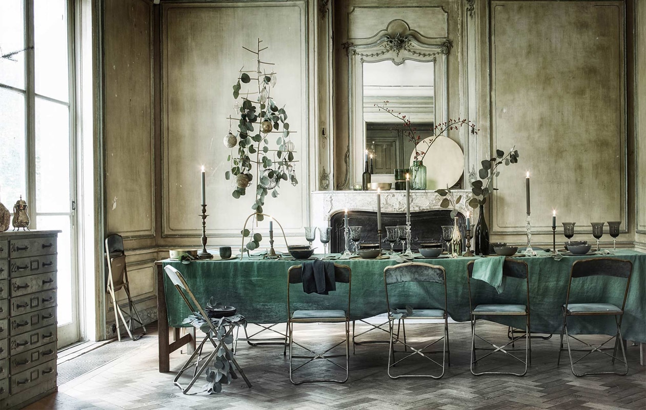 Lange eettafel gemaakt van Frans oud eikenhout 380x80x78 (). Klapstoelen bekleed met fluweel (). Koperen kandelaar ().  en , , , ,  als onderbord (www.vtwonen.nl). Linnen tafelkleed 350×160 cm, linnen servetten (). Borden, kommen (). Goudkleurige metalen kerstboom (). Groene glazen pot (). Waxinelichthouder met goudkleurige band ().