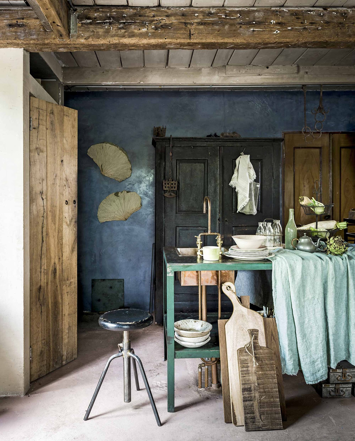 Kruk, kast prijs op aanvraag, houten snijplanken, kopje van Monki Ware, servies (). Waaiervormige bladeren aan de muur (), stapel borden (), jadegroen tafelkleed (), metalen etagère en glazen flesjes in rekje van Linda’s hoekje, koperen wasbak, koperen kraan op maat gemaakt (Jan van IJken), linnen theedoek (). Matglazen fles en tinnen theepot zijn privébezit. vtwonen 10-2016 | Fotografie Sjoerd Eickmans | Styling Liza Wassenaar