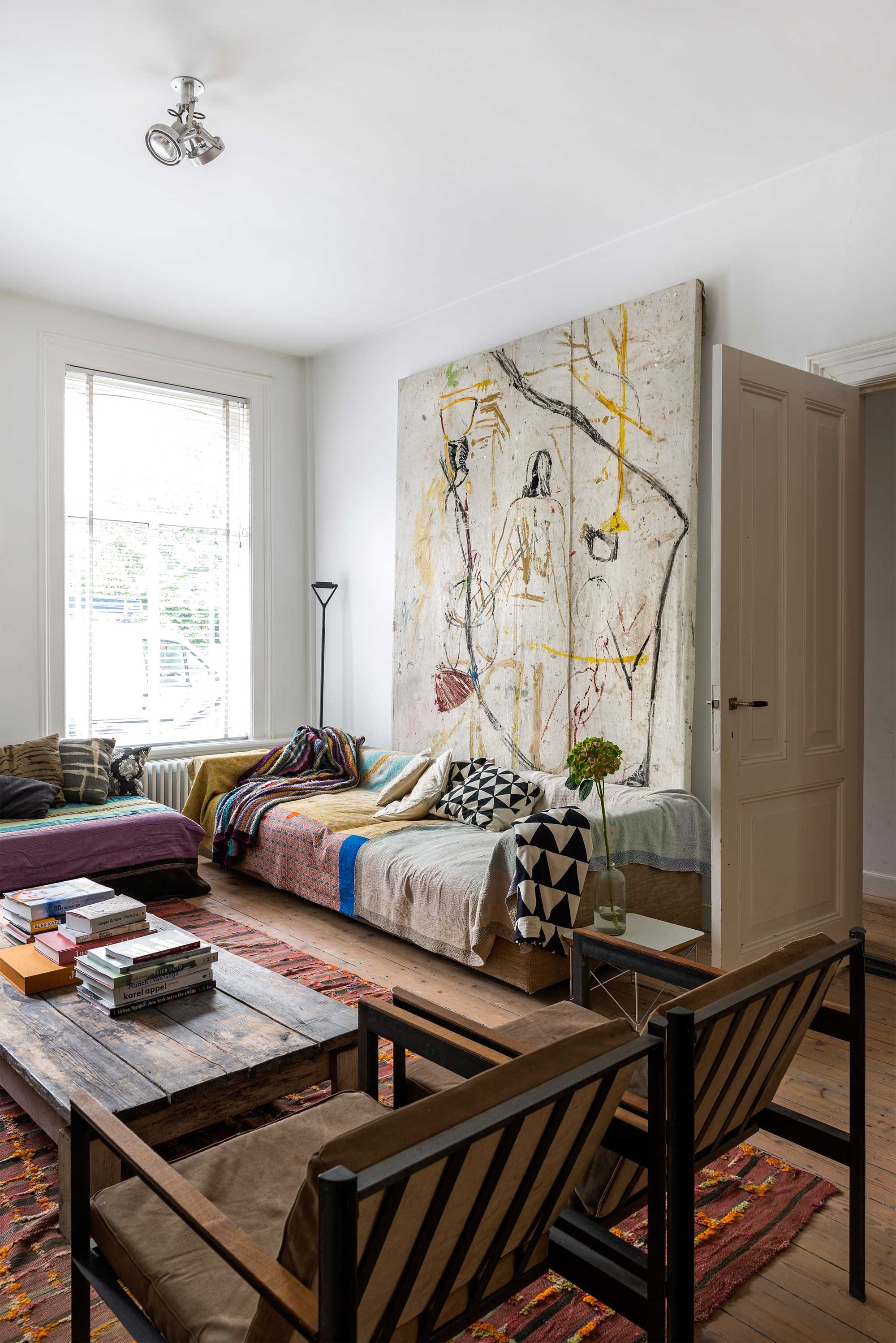 Vloerkleed meegenomen uit Marokko. Fauteuils van Loftstyles in Antwerpen. Achter de bank hangt eigen werk. Op de bank liggen quilts en beschilderde kussens uit Bali. Naast de bank een bijzettafel van Vitra. Plafondlamp van Artemide. De salontafel van steigerhout heeft jarenlang in de tuin gestaan. Jasper: ‘Toen de tafel de juiste verweerde uitstraling had, heb ik ’m verzaagd tot lage salontafel.’ vtwonen 10-2016 | styling Emmy van Dantzig | fotografie Stan Koolen