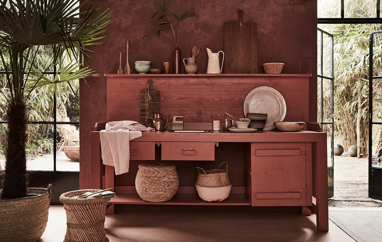Keuken met werkblad (Combitex). Mand (met palm erin), mand met deksel, linnen schort, houten schaal, houten lepels, gestreepte mand rechts op het keukenblad (Couleur Locale). Mand met roze bodem (Sissy-Boy). Houten planken, grote lila schaal, hoge kan, kommen (op werkblad), borden, linnen theedoek (Meker Wonen). Puddingvorm (De Weldaad). Koperen kan (All the Luck in the World). Roze beker (Six and Sons). Groene kommen (Serax). Houten bakje op plank (HK Living). Houten beker (Raw Materials). Bamboe kruk (Zenza). Bruine oude kan privébezit.[/caption] vtwonen 09-2016 | Fotografie Alexander van Berge | Styling Cleo Scheulderman