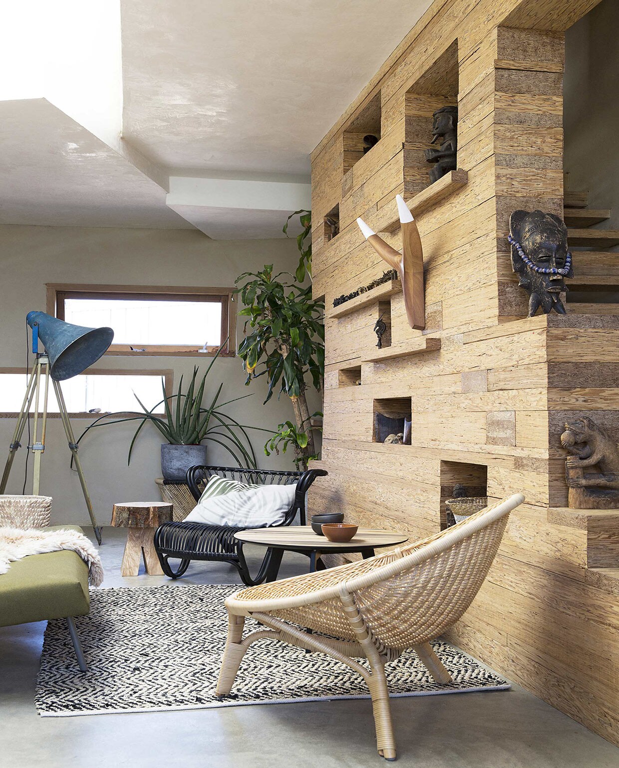 Wand langs trap, ontworpen door Nicky Zwaan en Joris Brouwers/House of Bouw, gemaakt van PSL (Parallel Strand Lumber) dat in de VS wordt gebruikt als constructiemateriaal in de huizenbouw, hier niet te koop (House of Bouw). Vloerkleed met zigzagpatroon van leer en katoen, gevlochten krukje Mudda Stool onder plant (Zenza Home). Stoel in voorgrond Rana Chair NO-13-CU naturel, stoel Viggo Boesen zwart V8-11-PS, eiken salontafel Slo Savon (Design 020). Kussen met palmbladprint (Store Without a Home). Mand Porcupine naast bank, nguni hoorns in wand (From Africa With Love). Kommen zwart en rood van Beate Snuka (Frozen Fountain). Staande lamp (Raw Materials). Blokkrukje (Neef Louis). Grijze pot (Tuincentrum Osdorp). Overig privébezit. vtwonen 08-2016 | Fotografie Jansje Klazinga | Styling Frans Uyterlinde