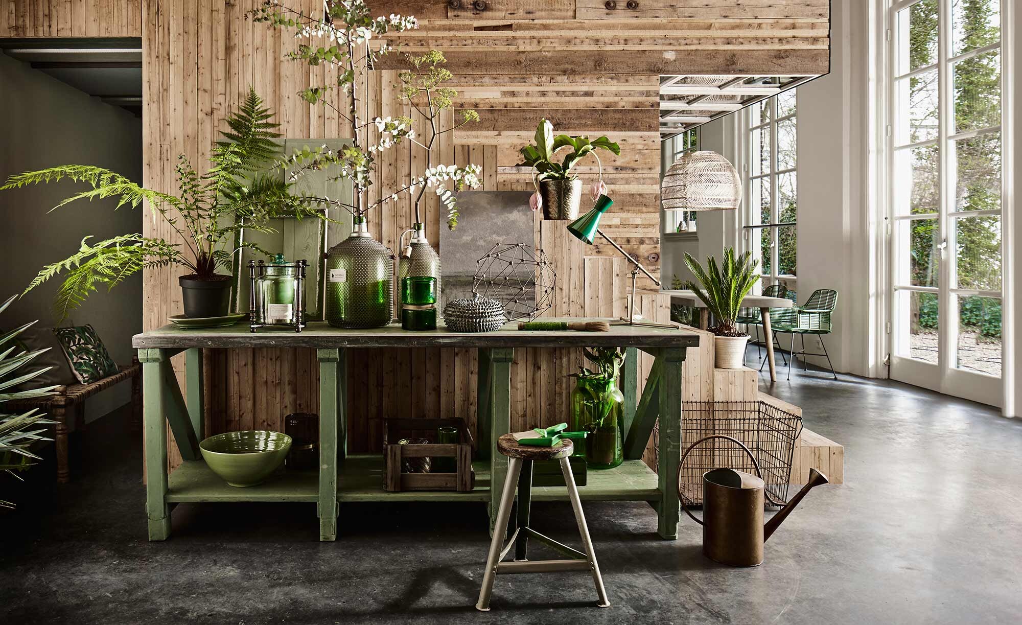 Werkbank, kruk, houten krat, hoge metalen mand, grote flessen met metaalgaas (Combitex). Gieter brons, pot met deksel en stekels (Maison NL). Grote aardewerken schaal, grote groene pot, glazen pot in houten frame, geometrisch object, groene ovale schaal onder plant (De Weldaad). Groene vaas met goud, bureaulamp Megaphone (Nordal). Stoffer en blik groen (l’Etoile Conceptstore). Chinese groene kwast (Zenza). Gevlochten bankje (Bodilson). Goudkleurige pot (H&amp;M Home). Overig privébezit.