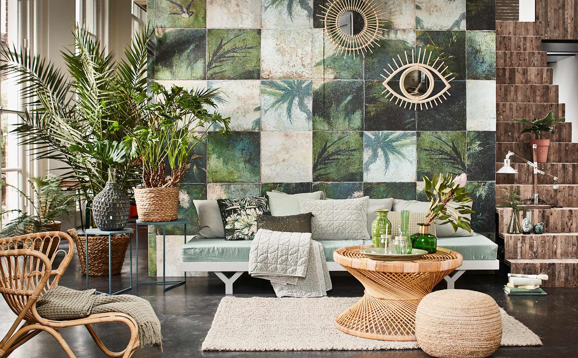 Vliesbehang Exotic Damier (Wall&amp;Decò). Daybed op maat gemaakt (Combitex). Rieten stoel Fox naturel, grijze kussens Deco Plain cotton van Tine K Home, vloerkleed Jute Twist, rotan tafel Palma (l’Etoile Conceptstore). Wafelplaid Coriander (Stapelgoed). Sidetableset Mimi Petrol, grijs kussen Vintage velvet, kussen Silver velvet, kussen wafel, groen kussen met pailletten, quilted plaid Shadow, flesvaas Knot met gehaakte buitenkant (Bodilson). Kussen bloemprint UNC Amazon Flower groen (Livv Lifestyle). Op de salontafel: groene schaal (De Weldaad). Groene glazen vaas met gouden hals, drinkglazen met deksel en rietje (Nordal). Groene aardewerken vaas (Six and Sons). Industriële lamp op de trap (Stapelgoed). Gevlochten poef, gevlochten mand op bijzettafel, uit set van 3 (Madam Stoltz). Grote gevlochten mand met palm (Nordal). Ronde spiegel met rotan rand, groene glazen karaf (Household Hardware). Spiegel in de vorm van een oog (Couleur Locale). Groene glazen vaas op trap (H&amp;M Home). Overig privébezit.