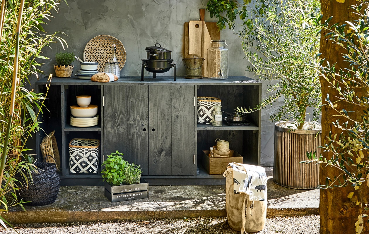 Geribbelde metalen plantenpot, ronde bus met deksel uit India (De Weldaad). Houten kruk, bamboe schalen met houten deksel, grote zwarte emaillen pan, kleine zwarte pannen, ecru borden, zwarte mand, naturel mand in kast set van 4, mandje met plant (Madam Stoltz). Glazen limonadetap, zwart-witte manden, witte emaillen borden, diepe borden, emaillen kommen, flesjes met zwarte dop en rietje (Nordal). Tafelkleed als schaduwdoek, schort, metalen kratje (H&amp;M Home). Laatje van metaal en hout (Burbri Antiek). Gevlochten schaal, houten kommen (HK Living). Barbecue Korpön (Ikea). Overig privébezit styling Cleo Scheulderman | fotografie Jeroen van der Spek