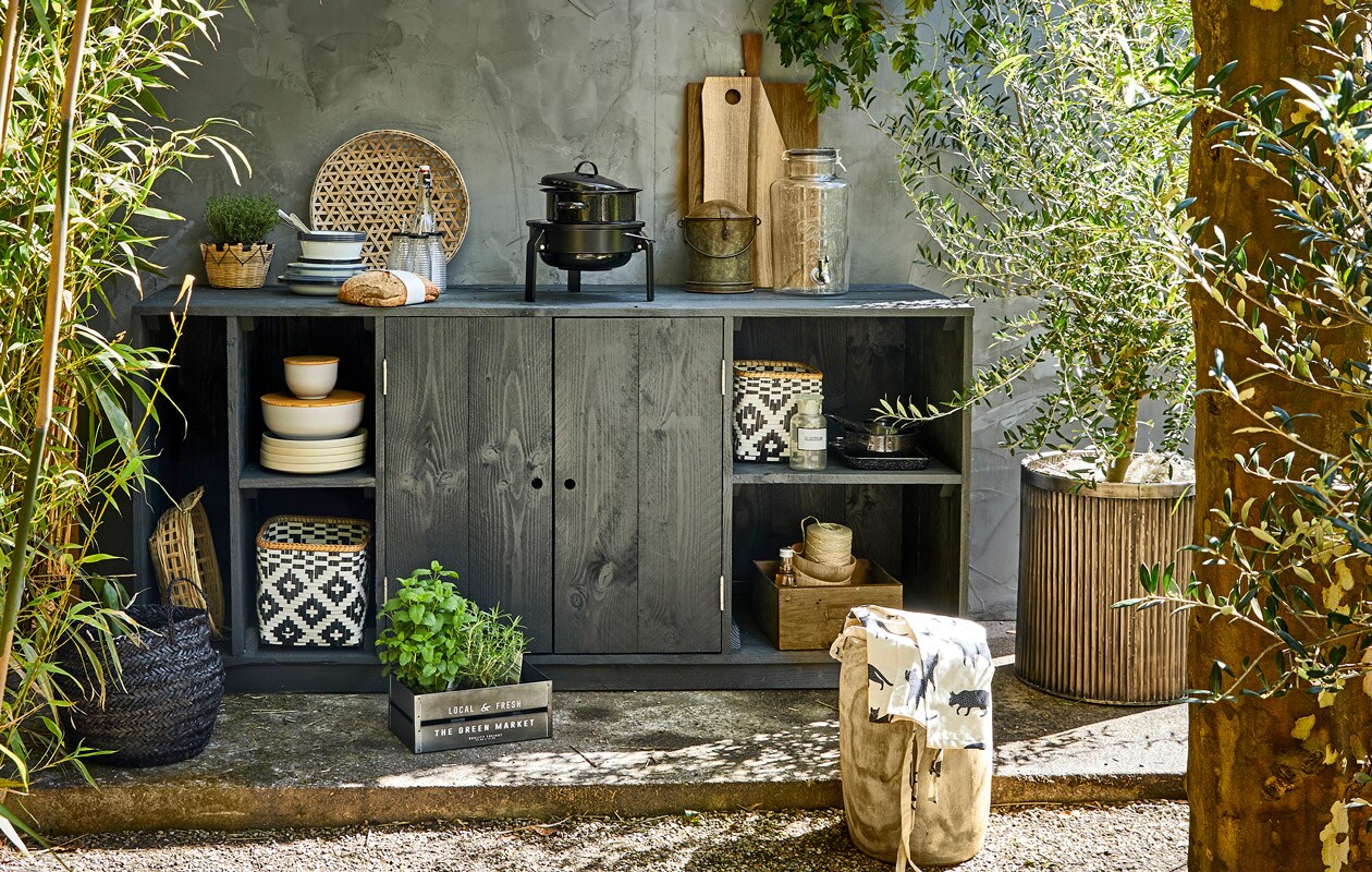 Geribbelde metalen plantenpot, ronde bus met deksel uit India (De Weldaad). Houten kruk, bamboe schalen met houten deksel, grote zwarte emaillen pan, kleine zwarte pannen, ecru borden, zwarte mand, naturel mand in kast set van 4, mandje met plant (Madam Stoltz). Glazen limonadetap, zwart-witte manden, witte emaillen borden, diepe borden, emaillen kommen, flesjes met zwarte dop en rietje (Nordal). Tafelkleed als schaduwdoek, schort, metalen kratje (H&amp;M Home). Laatje van metaal en hout (Burbri Antiek). Gevlochten schaal, houten kommen (HK Living). Barbecue Korpön (Ikea). Overig privébezit styling Cleo Scheulderman | fotografie Jeroen van der Spek