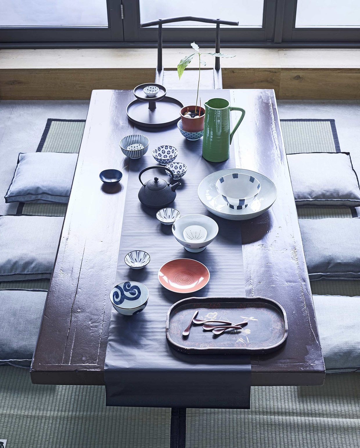 Tafel, geschilderd in kleur Chocolate van Little Greene (). Tafelloper gemaakt van zijdepapier (). Op de vloer tatamimatten (). Dienblad vooraan (). Etagère achteraan (). Groene kan (). Kom met streep, met bloem, met lijn en met krul, blauw, Japanse theepot van gietijzer (). Kommetjes Beijing Blue, klein schaaltje met stippen, rood bord (). Grotere schaal (). Kussens Lee (). vtwonen 05-2016 | Fotografie Jeroen van der Spek | Styling Fietje Bruijn