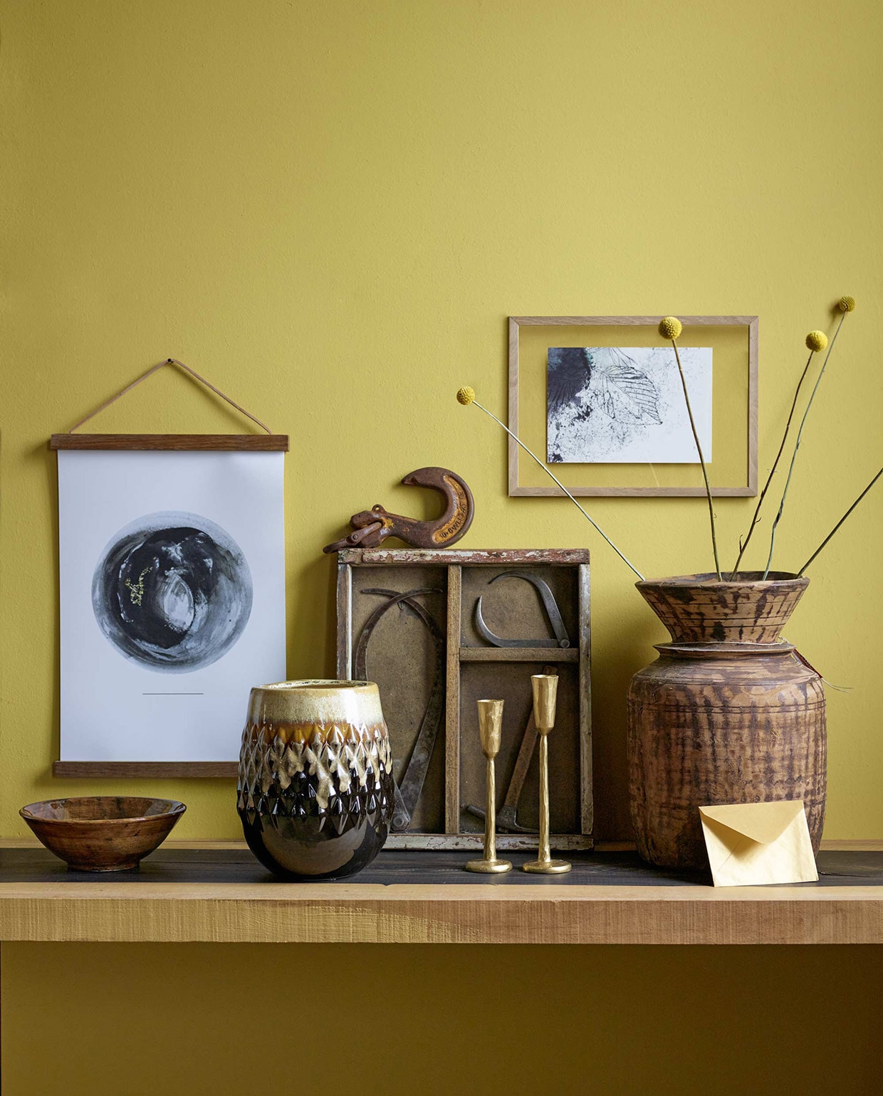 Muurverf Real Mustard uit de Pure collectie (Flexa). Ebbenhouten plank (Amsterdamsche Fijnhoutwinkel). Schaaltje, vaas van keramiek (Nijhof). Haak (Neef Louis). Kaarsenhouders van Madam Stoltz (deens.nl). Vaas (Hoffz). Glazen fotolijst vanaf A5, print Rondo van Studio Lianne Koster, frame van Ferm Living (Friday Next). In glazen frame een ansichtkaart inkt op papier (www.maartjevandennoort.nl). Houten kastje met gereedschap (Harvest &amp; Co.) is privébezit. vtwonen 01-2016 | Fotografie Tjitske van Leeuwen | Styling Marianne Luning