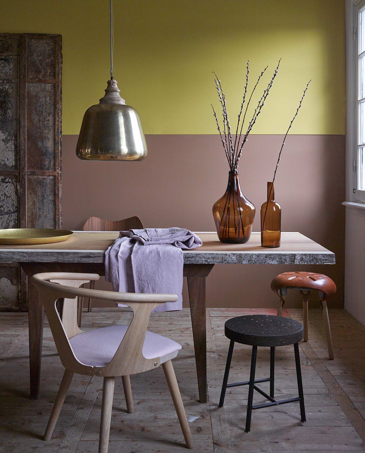 Muurverf (kalkmat) in de kleuren Real Mustard en Real Brown uit de Pure collectie, (Flexa). Tafel bestaande uit: dikke houten plank (Amsterdamsche Fijnhouthandel) en onderstel (privébezit). Krukjes met kurk zitting Sinnerlig (Ikea). Houten In Between SK2 stoel met gestoffeerd zitvlak van &amp;Traditionn, stoel serie 7 walnoot van Fritz Hanzen, kruk Paddle van Sjoerd Vroonland (Friday Next). Roze linnen tafelkleed (Sissy-Boy). Flesvaas smal, flesvaas groot (House Doctor). Goudkleurige schaal (Nijhof). Goudkleurige hanglamp van Madam Stoltz (www.deens.nl). vtwonen 01-2016 | Fotografie Tjitske van Leeuwen | Styling Marianne Luning
