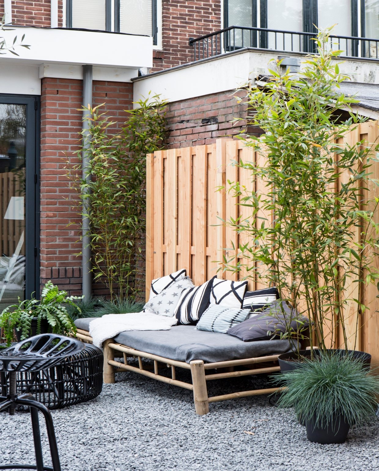 Terras met een bamboeloungebank met grijze en witte kussens en een houten schutting vtwonen 2017 | styling Cleo Scheulderman | fotografie Alexander van Berge