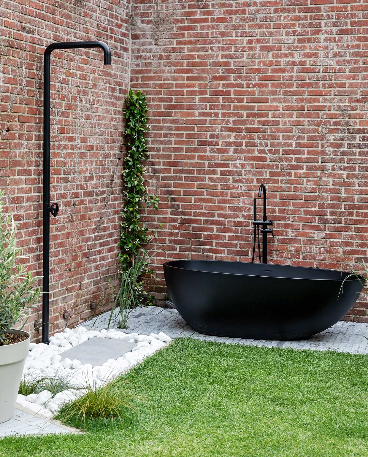 Vrijstaand ligbad matzwart composiet Solid Surface. Buitendouche Napoli Plieger, matzwart laten poeder-coaten. Hardstenen waaltjes Spotted Bluestone.Keramische staptegel 80×40 cm Cemento Grigio. Keien Crystal White van Tuincentrum Leurs. Overig onbekend. vtwonen 02-2022 | styling Ilona Jongepier | fotografie Dana van Leeuwen