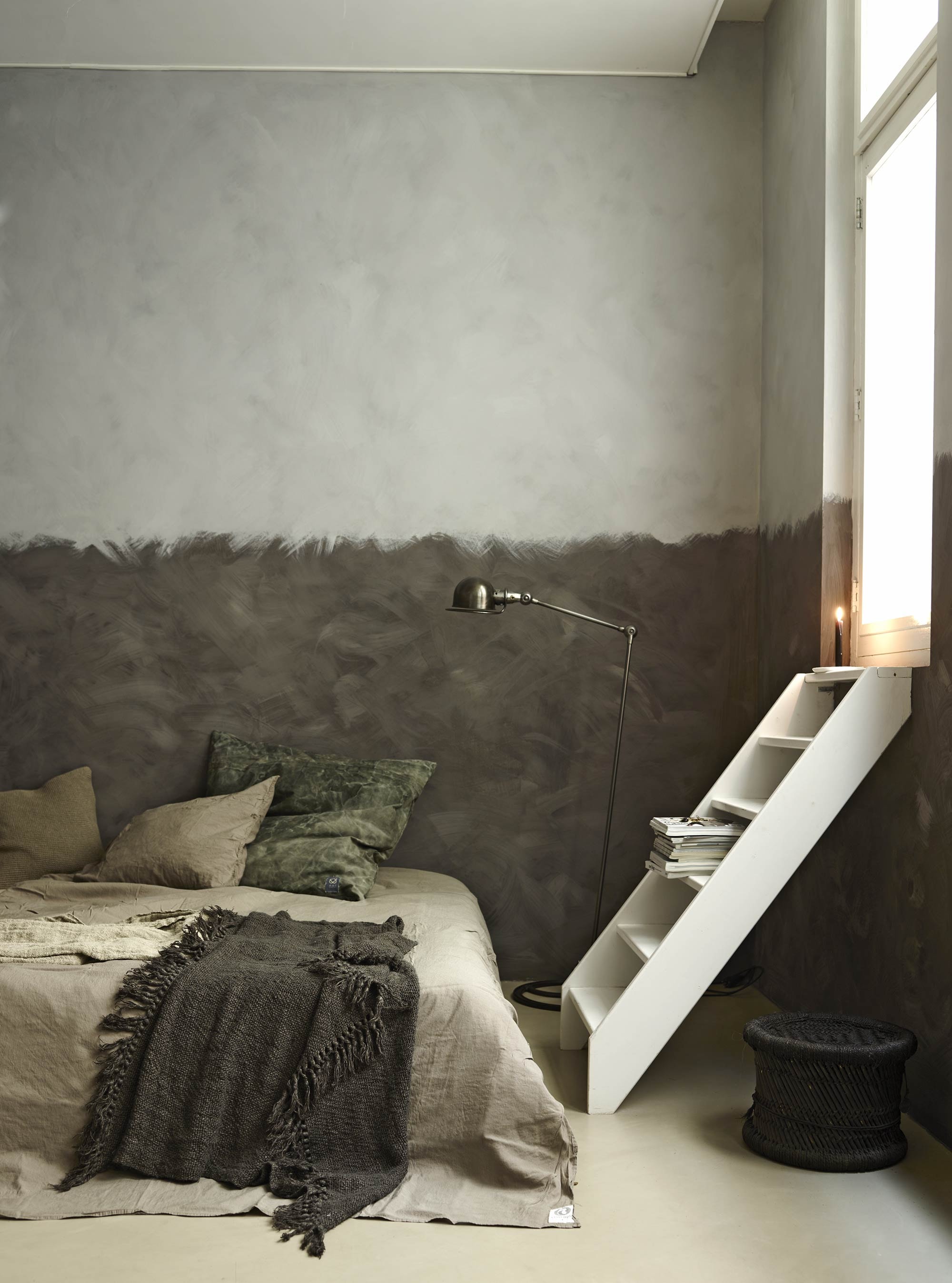 Lambrisering verf onderrand Blackthorn uit de Limestone collectie van Bauwerk, verf bovenkant Dove uit de Limestone collectie van Bauwerk, gerecycled grijs canvas kussen van Aai made with love, staande lamp van Harvest &amp; Co., sieraden op tijdschriften (AnoukB). Dekbedovertrek Momo in stonewashed linnen (vtwonen.nl). Kussen Chunky denim (Nijhof). Linnen plaid met bruine en grijze streep, donkergrijze linnen plaid, rotan krukje (Hoffz).