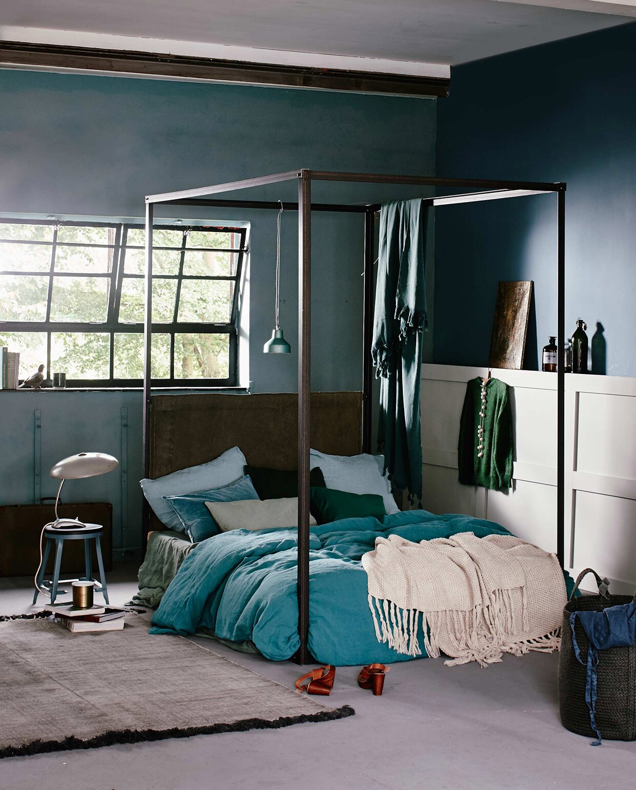 Hemelbed, op maat gemaakt (Combitex). Op bed: linnen kussensloop, linnen dekbedovertrek, 220×240 cm, linnen laken (Couleur Locale). Zeeblauw fluwelen kussen (De Weldaad). Twee groene kussenhoezen, gebreide beige plaid (H&amp;M). Kussen in lichtgroen canvas (Nordal). Hangende sprei (Hammam34). Hanglamp (Brût Amsterdam). Kruk (Madam Stoltz). Vintage leeslamp, schilderij op lambrisering, mand rechts vooraan (Six and Sons). Koffer, duif (De Weldaad). Groene gemarmerde beker (H&amp;M). Vloerkleed (Aai made with love). De muur bij het raam is geschilderd met muurverf Pure &amp; Original Classico krijtverf Blue Reef en de zijmuur in Libo Bay, lak op lambrisering van Pure &amp; Original Classico Oil Eggshell, kleur Silver Clay per liter (De Ru). Overig privébezit. vtwonen 11-2015 | Fotografie Jeroen van der Spek | Styling Cleo Scheulderman