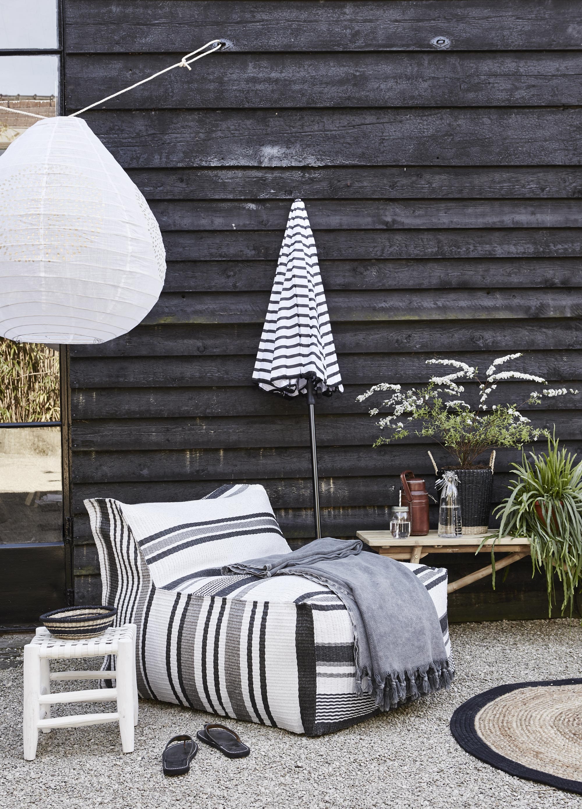 Stoffen lampion Berber Ufo, Ø 80 cm (It’s Loft). Witte kruk (Household Hardware). Mandje (H&amp;M). Buiten-fauteuil Lagoon van HK Living, plaid (vtwonen.nl). Gestreepte parasol (Livv Lifestyle). Bamboe bank van Tine K Home (l’Etoile Conceptstore). Mason Jar drinkbeker van Nordal, set van 4 (vtwonen.nl). Leren thermoskan (Meker Wonen). Glazen karaf van Bloomingville (vtwonen.nl). Rieten zwarte plantenmand met hengsels (H&amp;M). Vloerkleed van HK Living Ø 120 cm (vtwonen.nl). Slippers (Tierlantijn).