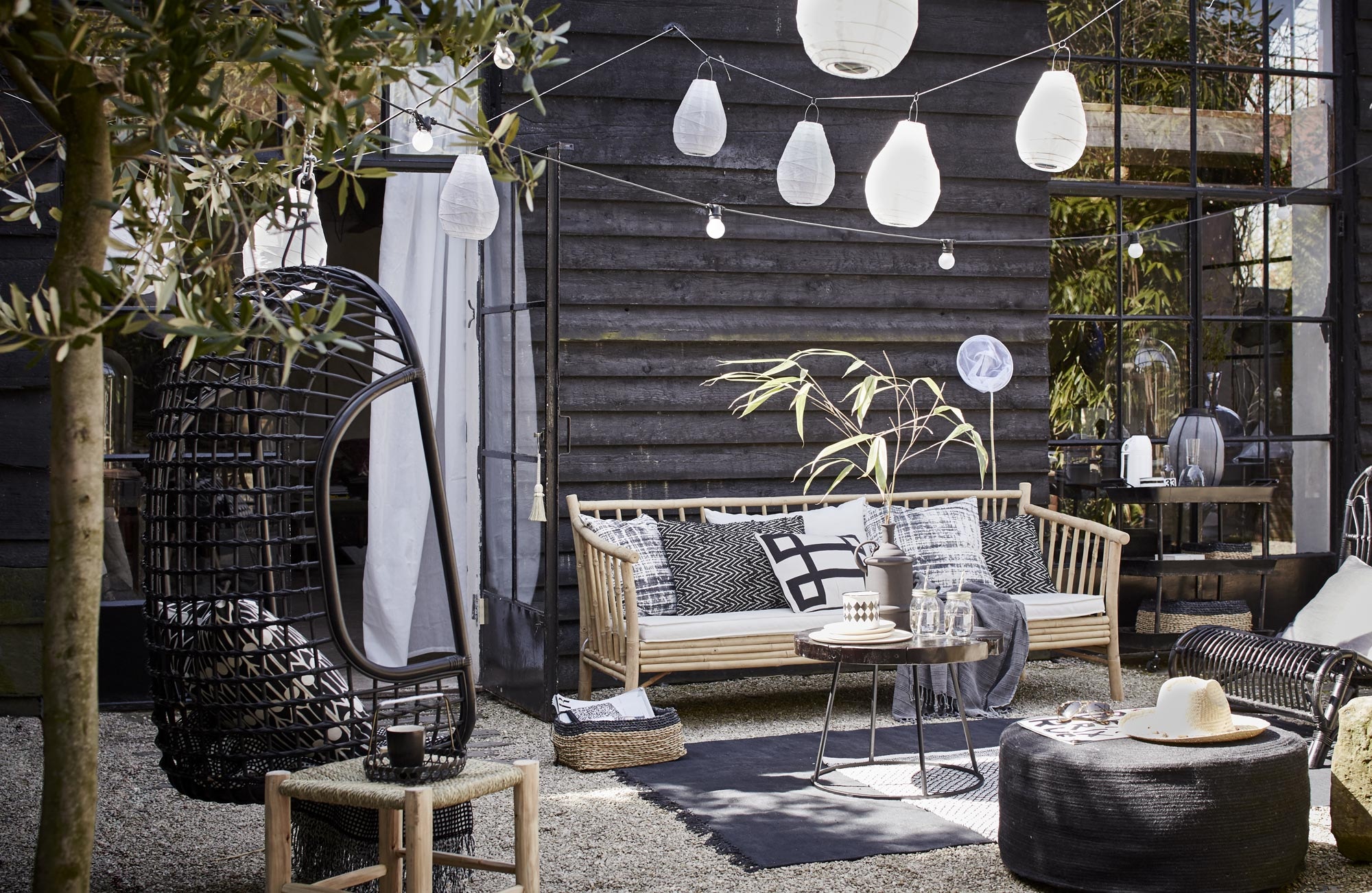 Bamboe bank van Tine K Home, 190 cm breed (l’Etoile Conceptstore). Kussens op de bank van linksaf: hoes met vervaagde ruit, Worn van House Doctor, 50×50 cm, zigzagkussen Graphy van Casa Vivante 60×40 cm, wit kussen met zwart grafisch motief Lifestyle Manhattan 50×30 cm (vtwonen.nl). Plaid (Hammam 34). Rotan hangstoel van HK Living (vtwonen.nl). Erin kussen Feathers van Littlephant, 50×50 cm (Livv Lifestyle). Plaid (H&amp;M). Marokkaanse gevlochten kruk van HK Living, groot 37x37x42 cm, klein 31x31x25 cm, salontafel Kraton van Dutch Bone, Ø 60 cm, matzwarte vaas van Madam Stoltz, juten poef van HK Living, 30×70 cm (hxØ) (vtwonen.nl). Mason Jar drinkbekers set van 4 (vtwonen.nl). Houten bordjes van HK Living, emaillen zwart-wit potje set van 2 (vtwonen.nl). Rieten hoed (Sukha Amsterdam). Vloerkleed Stack van House Doctor, zwarte rotan stoel van House Doctor (vtwonen.nl). Zwart-wit vloerkleed (H&amp;M). Lampions Drop van House Doctor, 30×20 cm (hxØ) per 2 en 35×24 cm (hxØ) per 2, lichtsnoer Bella Vista van Seletti, 10 lampen, 14,2 meter (vtwonen.nl). Visnet (Sissy-Boy Homeland). Gordijn set van 2 (Ikea). Rieten lage manden van Serax set van 3 (vtwonen.nl).
