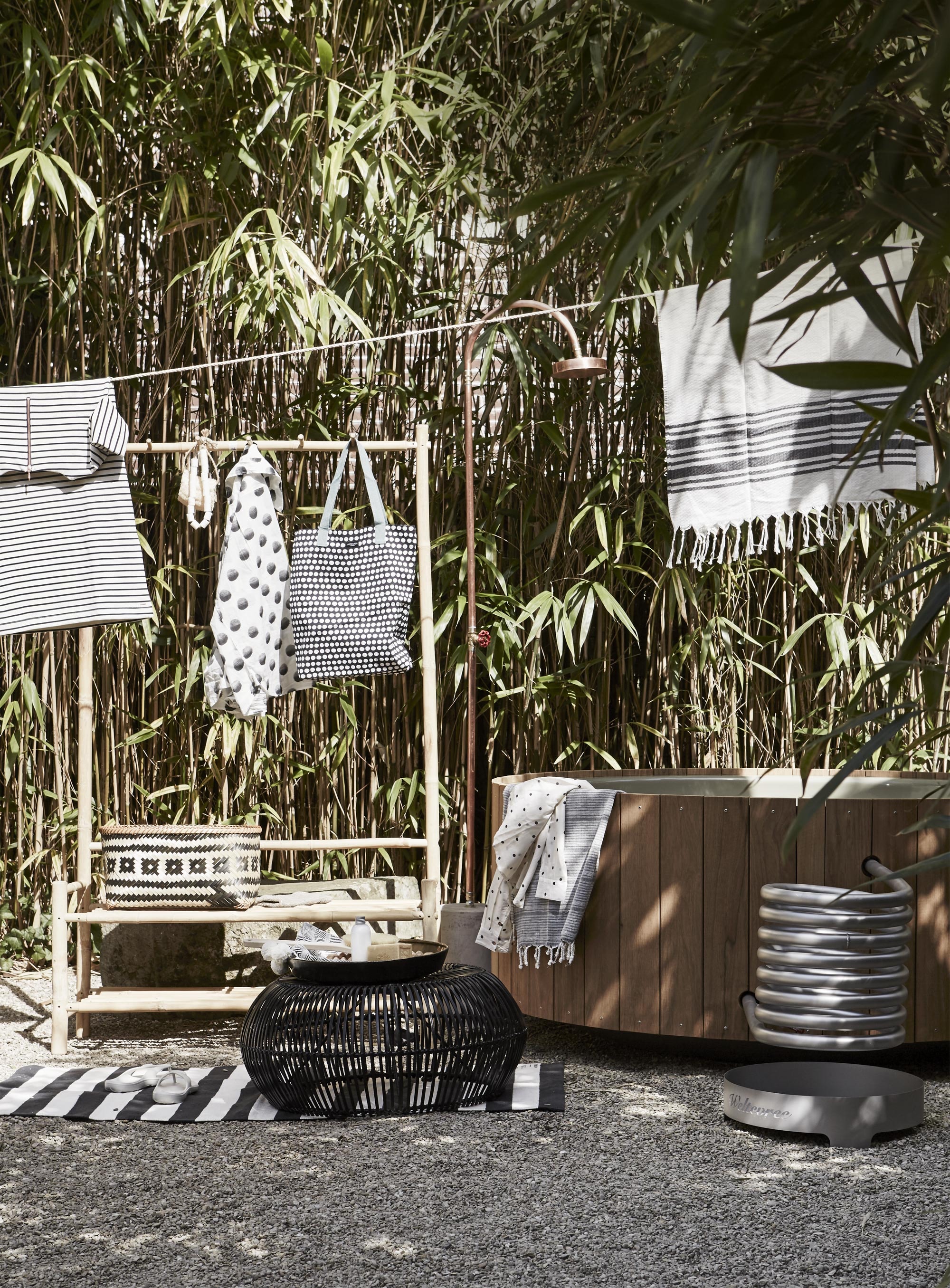Bamboe kledingrek van Tine K Home, 37 x 100 x 180 cm (l’Etoile Conceptstore). Buitendouche van Seletti (vtwonen.nl). Buitenbad Dutchtub Wood (Weltevree). Vloerkleed (H&amp;M). Rotan poef (Zenza). Aan de waslijn: gestreepte jurk (Sissy-Boy). Witte hamamdoek met zwarte streep (H&amp;M). Aan het bamboerek: zeepketting (Ottomania). Scrubhandschoen (Dille &amp; Kamille). Blouse met stippen (Ien Lifestyle Shop). Tas met stippen (Livv Lifestyle). Mand (Tierelantijn). Slippers van Aussie Soles (Tierelantijn). Op de poef: dienblad (Meker Wonen). Rugborstel, bodylotion , zeep (Dille &amp; Kamille). Over het bad: blouse met stippen (Ien Lifestyle). Hamamdoek (vtwonen.nl).