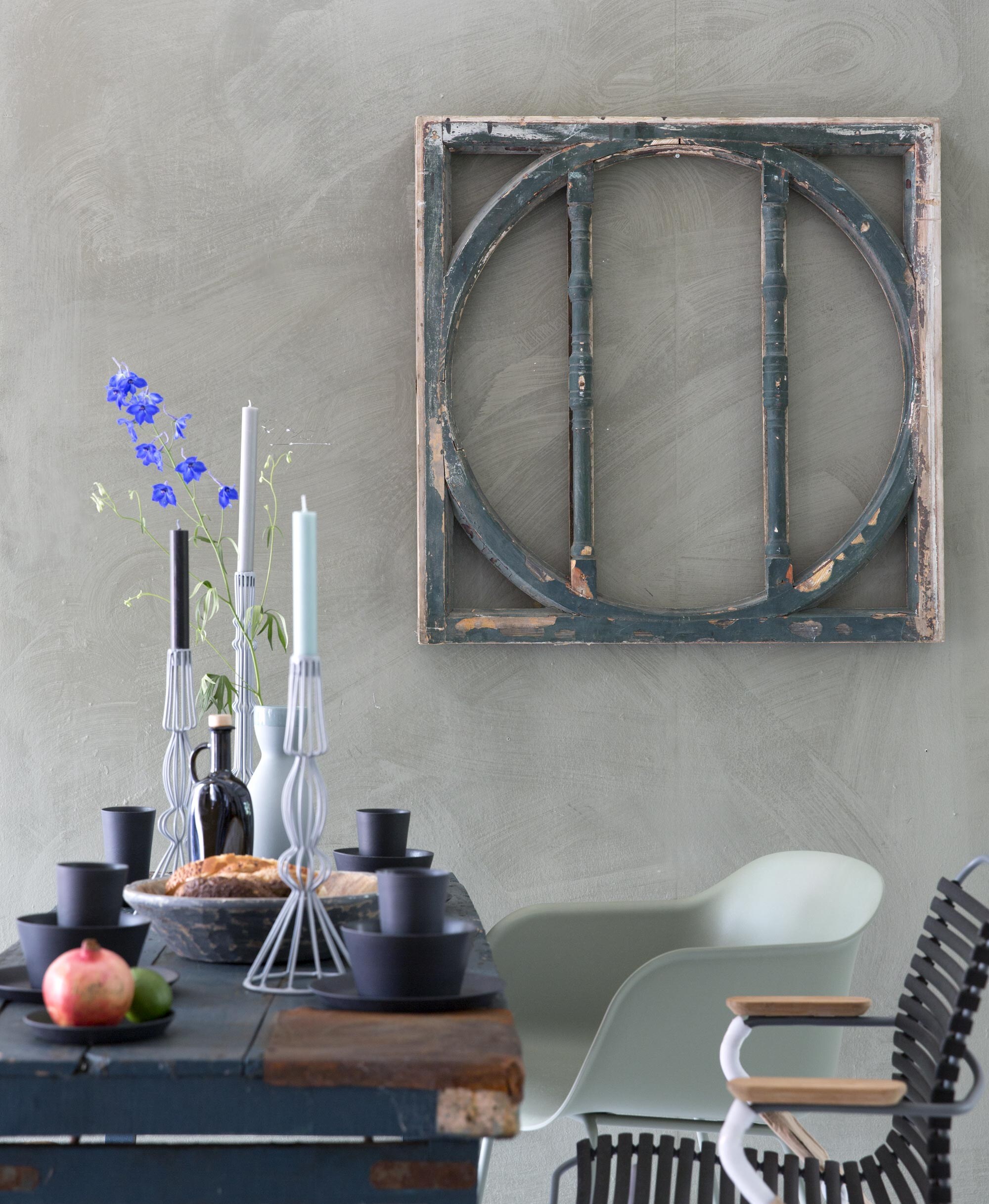 Raamkozijn (). Verf op de muur: Olive van Bauwerk lime paint (). Muuto fiber chair groen (). Houe Clic  (Anno Design). Zwart bamboe servies, 12-delig (). Karaf van Carola Zee (). Grijs metalen kaarsenstandaards (). Kaarsen (). Olijfolie (Durf). Tafel, houten slabestek en bak privébezit.