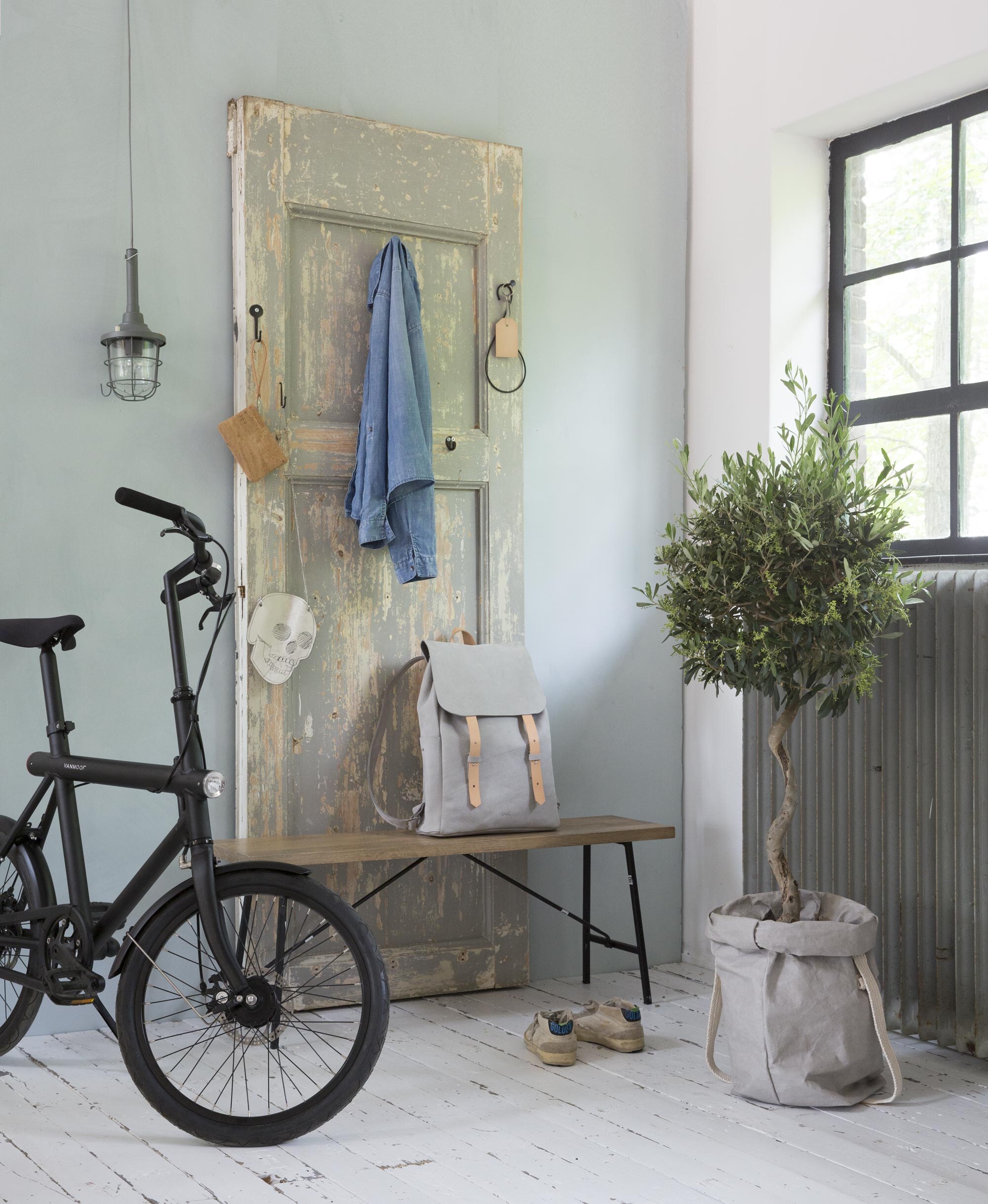Deur (). Verf op de muur: Verveine van Bauwerk lime paint (). Zwarte haken ().  van kurk Journey (www.pucbag.nl). Tasje Skul (). Sleutelhanger, rugtas ().  van Bepurehome (Basiclabel). Plantenzak van wasbaar papier ().  (Van Moof). Hanglamp van It’s About Romi ().