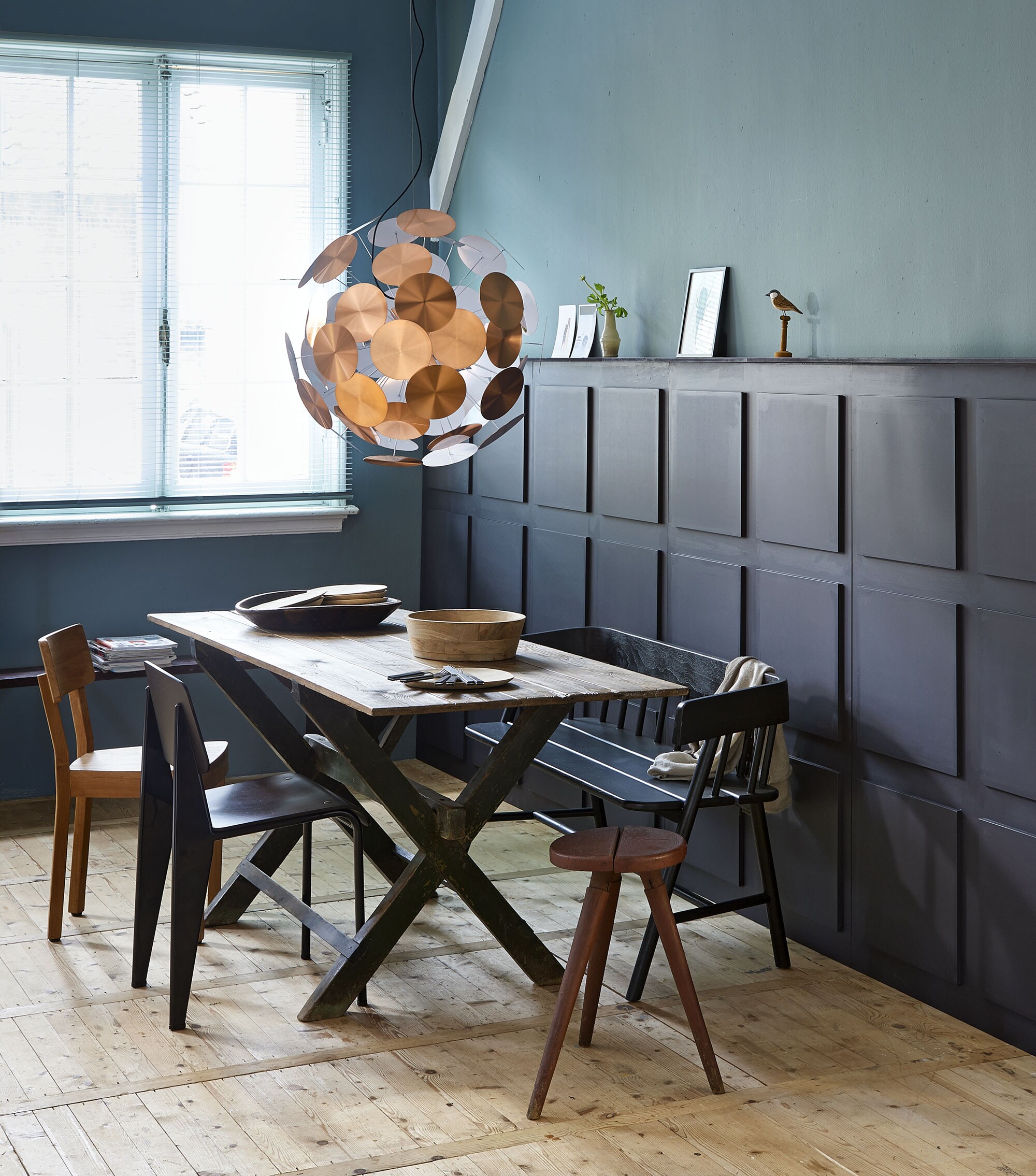 Houten tafel 85×195 cm, houten bankje zonder leuning (van Dijk &amp; Ko). Lichtgekleurde houten stoel (DR Wonen). Zwarte stoel van Jean Prouvé (Vitra). Krukje Red Stool (Blom &amp; Blom). Houten bank met leuning (HK Living). Lamp met koperkleurige schijven van Zuiver, mangohouten borden, lage houten schaal van HK Living (vtwonen.nl). Hoge houten bak, glazen vaasje (Nijhof). Bestek Mogen, 24-delig (Ikea). Kever in lijstje, houten vogeltje (De Weldaad). Muurverf per liter kleur Blue Reef, lambrisering kleur Fondant (Pure &amp; Original).