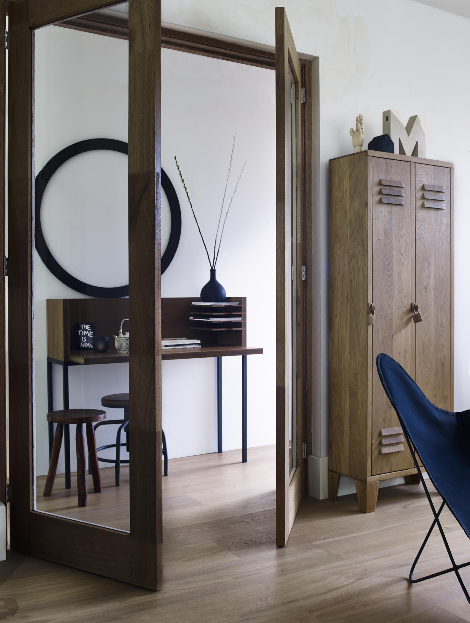 Lockerkast Locky van geolied massief eiken 66x180x30 cm (lxhxb) (). Bureau Wilke van gerookt eiken 120x60x107,5 cm (). Houten kruk (). Kruk met stalen onderstel (vtwonen.nl). Letter M als onderdeel van set HOME (). Houten hand van Hay vanaf (). Houten huisje, theepot, zwarte vaas (). Mok (). Ronde houten lijst vanaf (). Vlinderstoel ().
