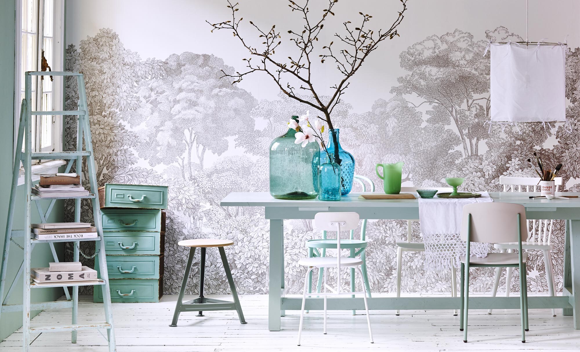 Kruk (). Stoelen achterin van links naar rechts: mintgroene caféstoel A18 Azur (). Witte schoolstoel van Galvanitas S.16 (). Spijlenstoel Sit (www.vtwonen.nl). Stoel links voor: Afternoon Dining Chair van Menu (First or Second). Stoel rechts voor van Vitra (). Behang Belwood van Rebel Walls per m² (). Eettafel vanaf (). Grote kruikvaas (). Kleine kruikvaas (). Turquoise vaas erachter (). Jadegroene kan, groen glas, schaaltje, tafelloper (). Houten broodplank (). Groen bord ().  Ø 50 cm (vtwonen.nl). Ladder ().