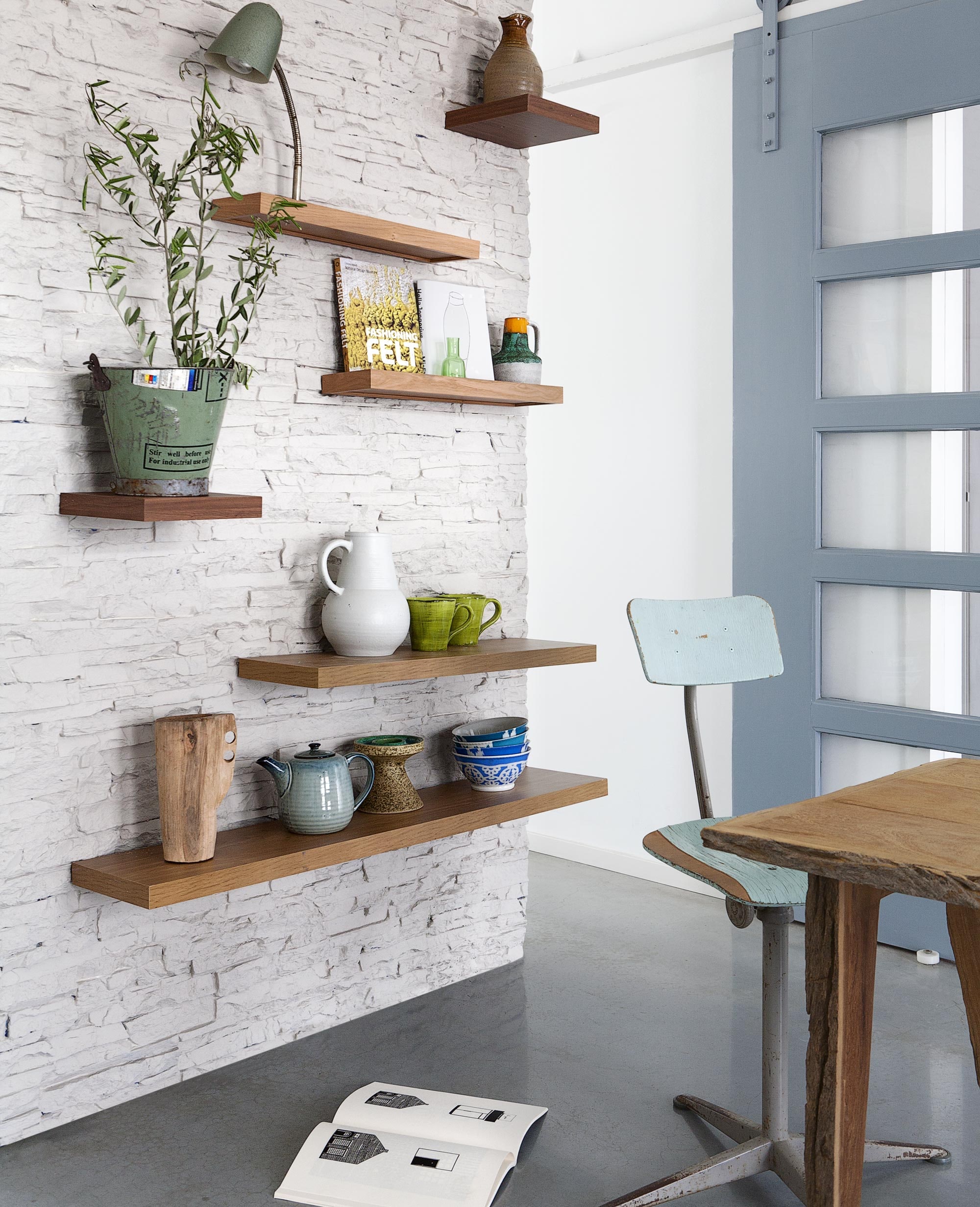Schap, kleine plank, middelste plank, grote plank (). Deze planken zijn gemakkelijk te bevestigen. Je monteert een metalen frame op de muur en schuift daar de plank overheen. Wandpaneel imitatie natuursteen 285×130 cm (). Van links naar rechts, van beneden naar boven: houten vaas (). Theepot, kandelaar (). Oezbeekse kommen (). Grijze kan (). Groene bekers Mamma Ro (). Boek Fashioning Felt, boek Misfit (). Glazen vaasje (). Vintage vaasje (). Lampje (). Bruin vaasje (). Stoel (). Tafel Bark (). Boek op de grond Binnenskamers van Tim Enthoven (). Plant privébezit.
