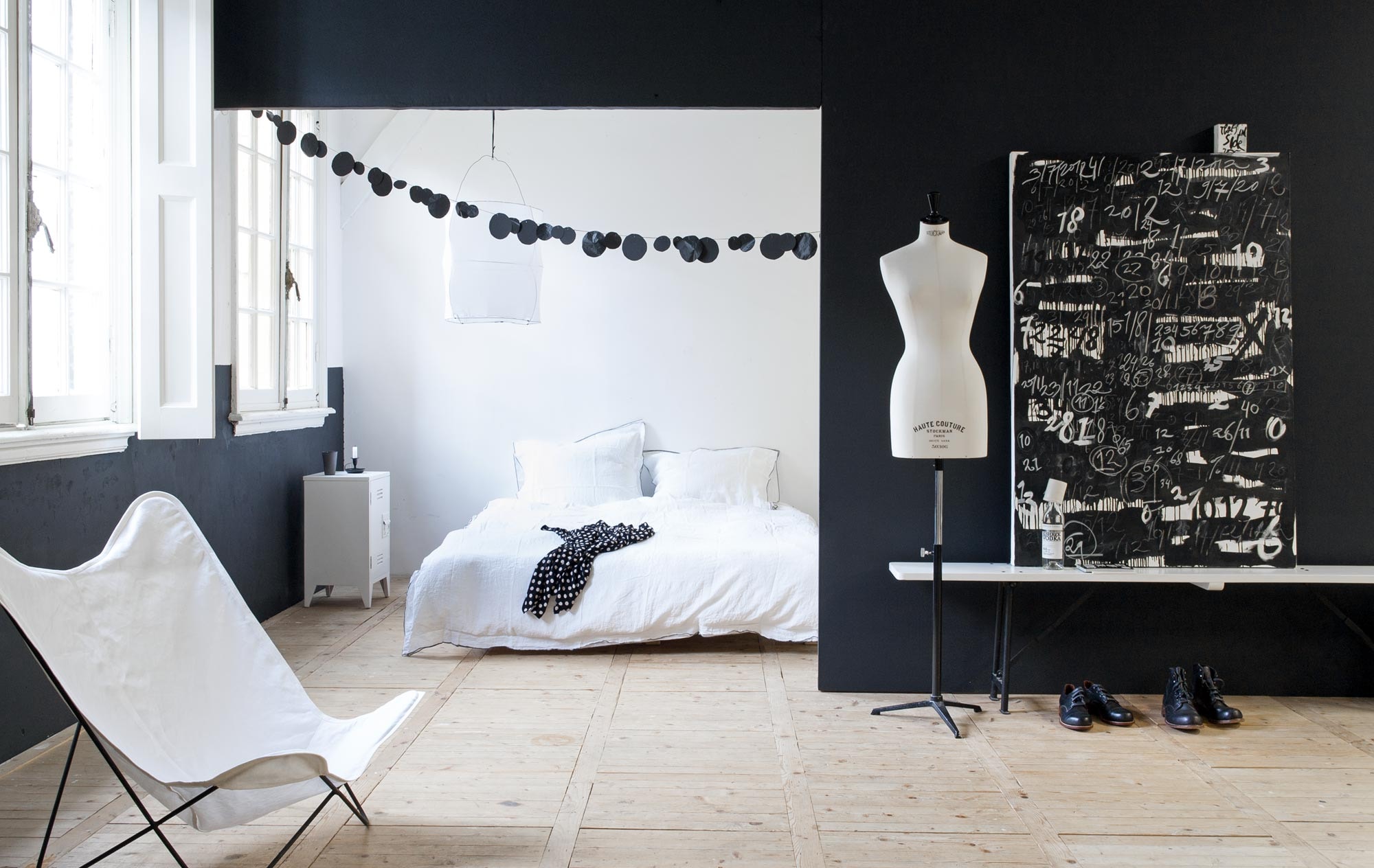 Kunstpaneel 6 Months 100×150 cm, erop klein schilderij Letters to my future 10×10 cm (Studio Lisette de Zoete). Op de muur muurverf Black en White per 2,5 liter (Farrow &amp; Ball). Vlinderstoel (Household Hardware). Bankje (Nijhof). Nachtkastje (HK Living). Dekbedovertrek wit linnen met zwarte piping van Wolterink (House In Style). Kaarsenstandaard (&amp;Klevering). Handgevormde mokjes (Belinda Parten). Stippenblouse (Summum). Schoenen (van Gils en Boohoo). Wodka (Bishkek). Paspop privébezit. Slinger zelfgemaakt.