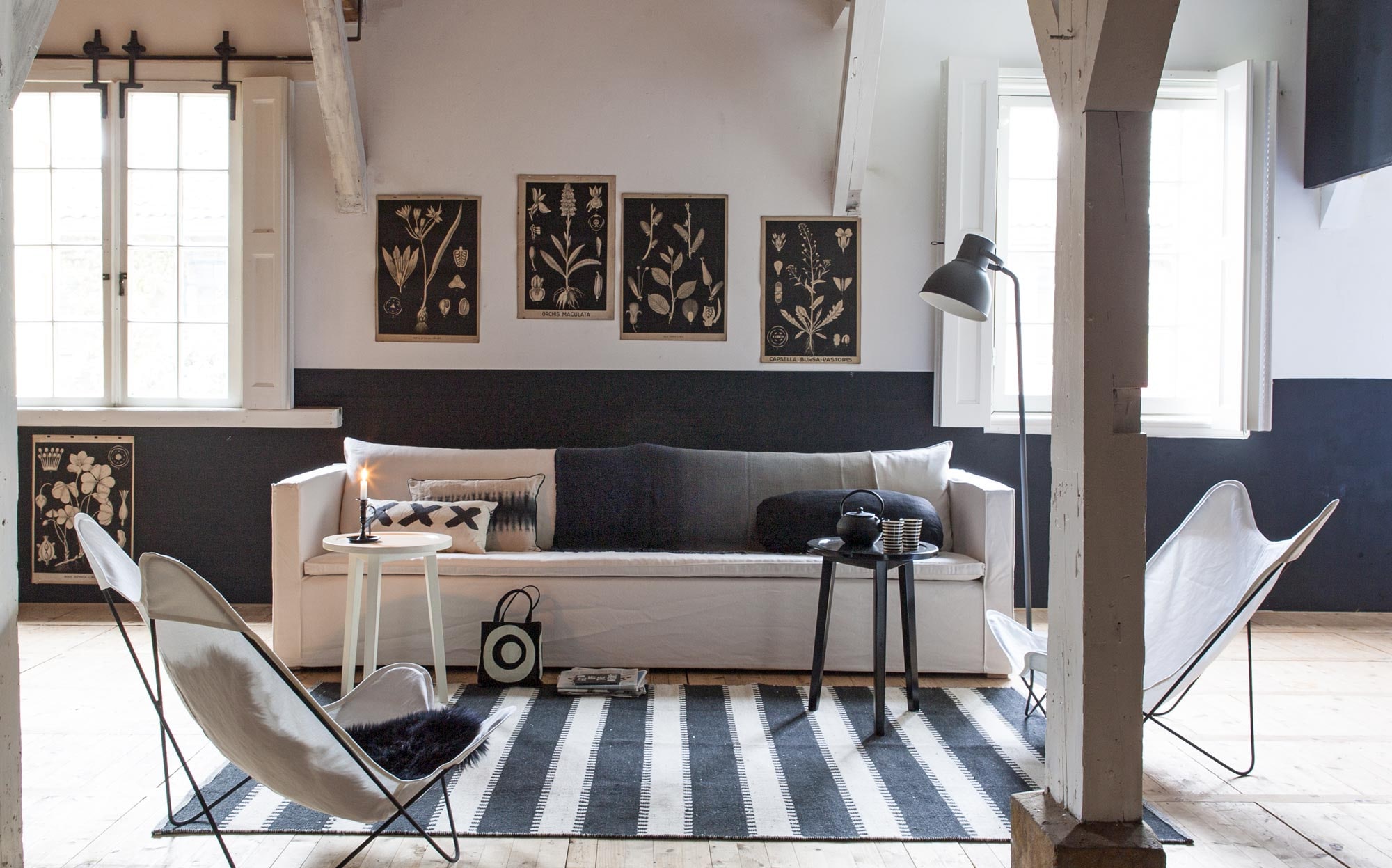Bank Phantom (Tine K Home). Tafeltjes uit de collectie van vtwonen (Nijhof). Vlinderstoelen (Household Hardware). Bekleding gemaakt van stof Hot Medicine (Chivasso). Vloerkleed 200×300 cm, linnen plaid met kleurverloop van Designers Guild (Wilhelmine van Aerssen). Lamp (Ikea). Oude botanische prenten op linnen prijs op aanvraag (Het Grote Avontuur). Schapenvacht (Het Kabinet). Kussen met kruismotief (HK Living). Kussen met tie die motief (Tine K Home). Kussen ovaal gemaakt van stonewashed linnen stof in zwart (Chivasso). Gevuld met dons (Jonk). Kandelaar (&amp;Klevering). Gestreepte mokken (Tine K Home). Theepot (Nijhof). Tasje privébezit.
