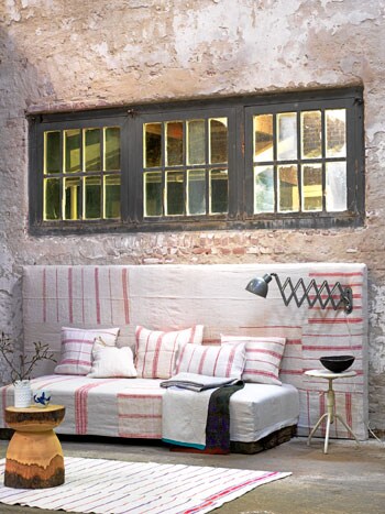 beeld vtwonen Een zelfgemaakte bank van een bed enlosse kussens. De boxspring, kussens en het hoofdeinde erachter zijn gestoffeerd met stukken oude boerenstof en effen linnen. Doordat het hoofdeinde net zo breed is als de raampartij erboven, oogt het mooi afgestemd.