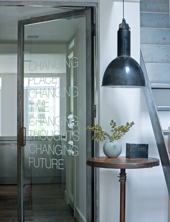 beeld vtwonen De glazen deur is omlijst met een stoer stalen frame en verfraaid met een even stoer gedicht. De deur is van Kodde Architecten, de tafel van Fens Decor en de lamp van neef Louis. Fotografie Bob Eshuis.
