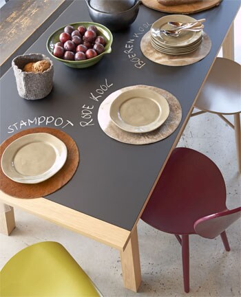beeld vtwonen Middelpunt in de eetkeuken is een naturel tafel met 'schoolbordblad' (Kok Wooncenter), omringd door comfortabel Zitmeubelende stoelen van gebogen hout Linteloo), in de kleur van wintergroenten. Het servies lijkt van ambachtelijk aardewerk, maar is vaatwasmachinebestendig porselein. Wel zo makkelijk. Heel creatief; de koeienhuiden placemats zijn eigenlijk stoelzittingen (Gilbert)! Fotografie Paul Grootes.