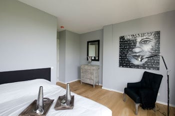 beeld vtwonen Altijd goed: zwart-wit. In deze slaapkamer zijn zwart en wit gecombineerd met lichtgrijze muren en een houten vloer. Tegen de muur komt het kunstwerk extra goed uit. Het geheel oogt als een stijlvolle hotelkamer. Fotografie Jeroen Scheelings.