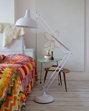 beeld vtwonen Naast het bed staan twee plectrumvormige tafeltjes, gekocht bij de kringloopwinkel. De uitvergrote bureaulamp is te koop bij Pol's Potten. Van een hardboardplaat met gaatjes is een muur decoratie gemaakt: hij is wit geverfd en volgens is er een bloem op geborduurd. Fotografie John Dummer.