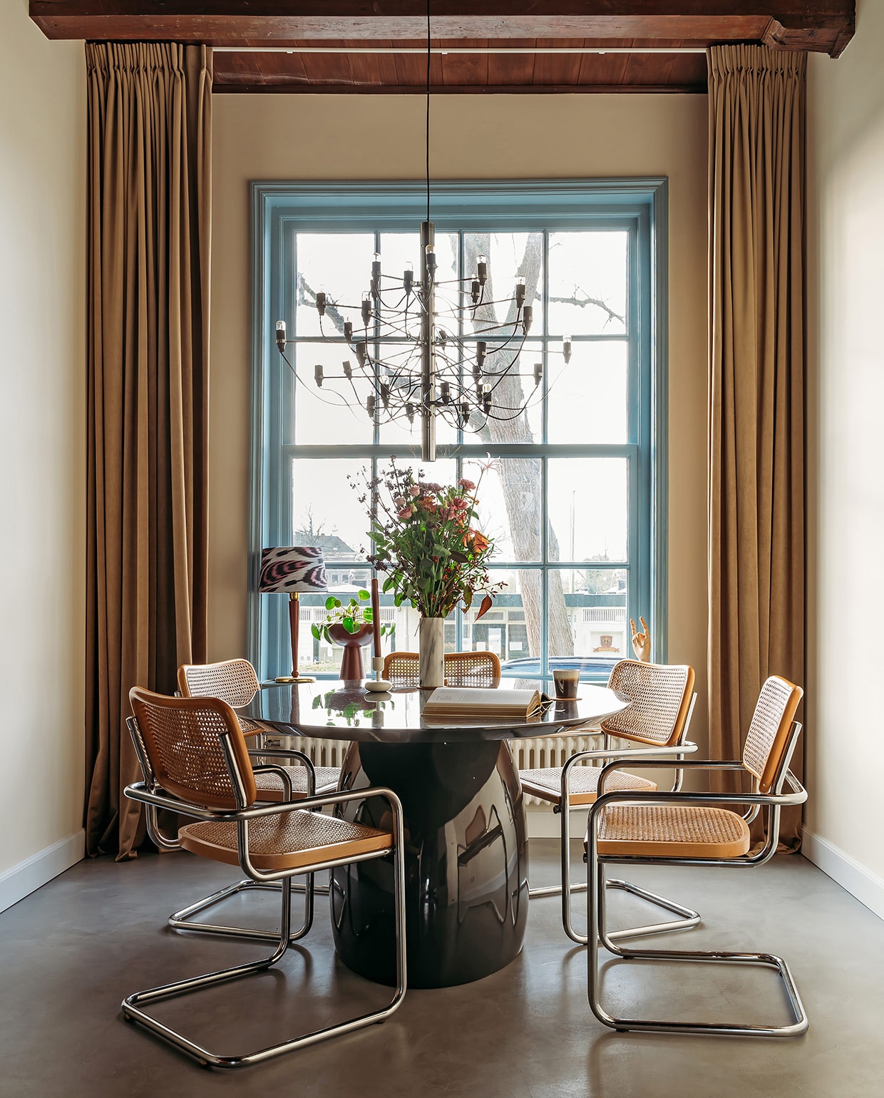 Vouwgordijnen Jan Sikkes, muurverf Inchyra Blue van Farrow &amp; Ball. Bank Rofra Home. Kussens, vloerkleed, poef en kandelaar Nox Studio Interiors. Bijzettafels Classicon, geurkaars, staande lamp Zara Home.Koffietafelboek Kelly Wearstler. vtwonen 03-2021 | productie Coco Features | styling Laurien Deken | fotografie Inge Korver