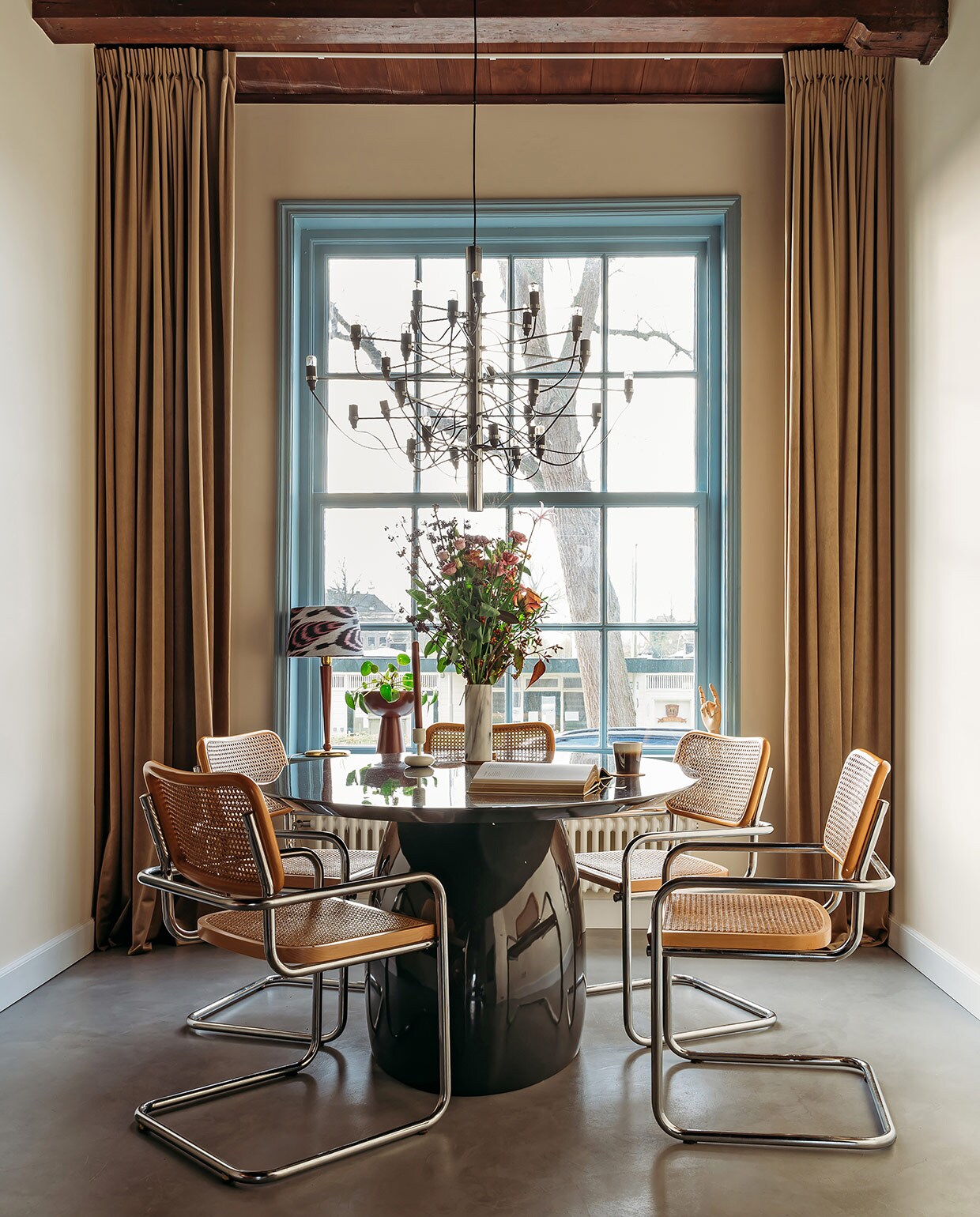 Vouwgordijnen Jan Sikkes, muurverf Inchyra Blue van Farrow &amp; Ball. Bank Rofra Home. Kussens, vloerkleed, poef en kandelaar Nox Studio Interiors. Bijzettafels Classicon, geurkaars, staande lamp Zara Home.Koffietafelboek Kelly Wearstler. vtwonen 03-2021 | Productie Coco Features | Styling Laurien Deken | Fotografie Inge Korver