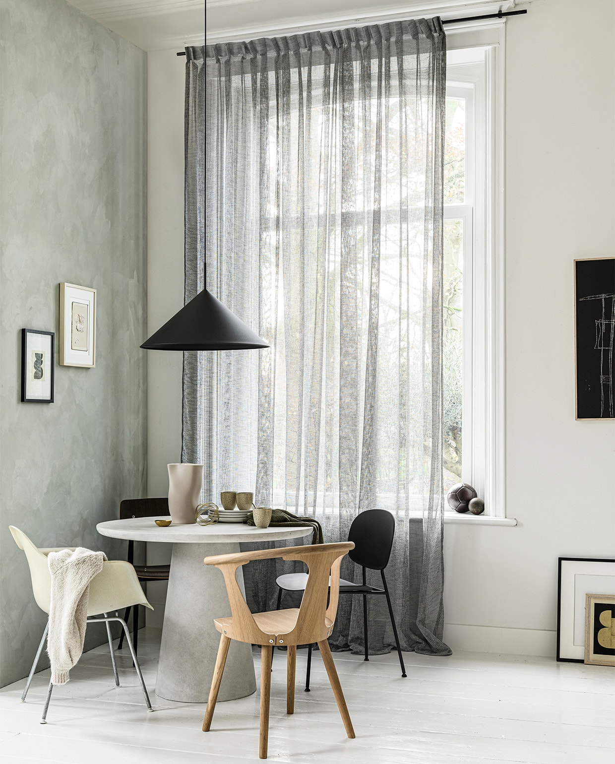 Gordijn op maat in stof Weave kleur 2712. M.m.v. basiclabel.nl (betonlook tafel Damon), demachinekamer.nl (Eames-stoel), loods5.nl (stoel In Between van &amp;Tradition, zwarte stoel rechts van Menu, zwarte stoel links Result van Hay), hkliving.nl (lamp, mokken, zwart kunstwerk), EawyArt via etsy.nl (kunstwerk in zwarte lijst), wonderwallstudios.com (kunstwerk in lichte lijst), hm.com (theedoek), vestingh.nl (kalkverf Smoking Glass). Overig privébezit. vtwonen 13-2020 | styling Marlies Does | fotografie Sjoerd Eickmans | productie Tanja Saarberg