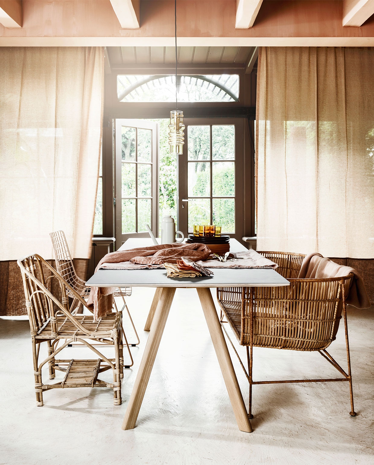 Gordijnen van linnen Sutton House van Chivasso per meter € 144,50 (jab.de). Tafel van Hay, 250×90 cm € 1389,-, rotan bank, 140 cm breed € 726,-, stoel Wire in roze € 169,-, stoel van bamboe van Madam Stoltz, € 230,95, amberkleurige lamp van Normann Copenhagen € 200,- (vtwonen.nl). Op tafel: koffiepot van Normann Copenhagen € 80,50, roze bord vanaf € 9,95, donkerrood bord € 16,50 (vtwonen.nl). Onderste tafelkleed van zachtroze linnen € 95,-, gele servetten per twee € 14,95 (hkliving.nl). Overige servetten € 10,- (gabrielle-paris). Tafelkleed van terrakleurig linnen € 150,- (weldaad.com). Messingkleurig bestek € 21,99 per driedelig couvert (nordal.dk). Plaid van Hay € 75,- (eijerkamp.nl). vtwonen 08-2019 | styling Marianne Luning | fotografie Stan Koolen