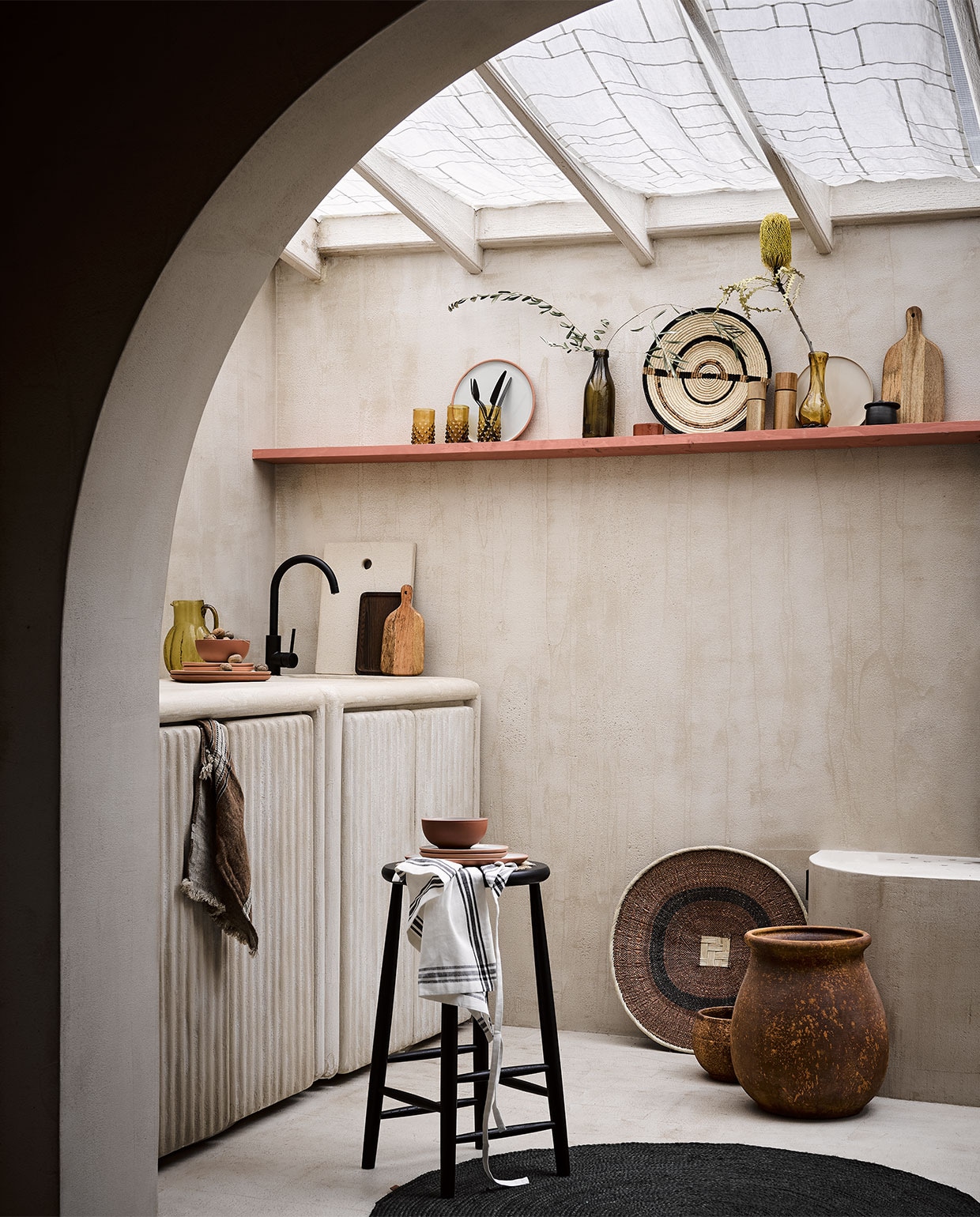 Linnen gordijnsheets gemaakt met pojagi techniek, prijs op aanvraag (bymolle.com). Plank geverfd in lakverf kleur Book Room Red No. 50 van Farrow &amp; Ball, per 2,5 liter € 97,- (deruamsterdam.nl). Zwart bestek Stella van Blomus op plank, 16-delige set € 129,99, acaciahouten peper- of zoutmolen van AdHoc, 17 cm (h) € 29,99, 14 cm (h) € 24,95, beige bord Terres de Reves in Misty Grey van Serax, 22 cm (Ø) € 18,40, dienblad Heii van Serax, 25×16 cm € 26,95, zwart rond vloerkleed Eternal van Ferm Living, 120×120 cm € 94,50 (vtwonen.nl). Microcement stuc op wand en vloer, prijs op aanvraag, inbouwkeuken met kraan per unit, vanaf € 2000,-, gestuukt dienblad tegen achterwand € 75,-, grote bruine vaas op de grond € 149,95, kleine bruine pot € 62,50, terra servies met groene binnenkant, schaaltje € 11,95, ontbijtbord € 14,95, groot bord € 16,95, klein terra schaaltje op plank € 14,95 (lanena-home.com). Houten snijplank groot € 12,99, klein € 9,99, wit schort met zwarte streep € 7,99 (hm.com). Droogbloemen (plantje.nl). Amberkleurig glas op plank met tak, per stuk € 13,-, mosterdkleurige fles met olijftak € 39,-, mosterd-kleurige glazen vaas met sierlijke vorm € 99,-, zwarte suikerpot € 47,-, mand met witte rand op grond, 58 cm (Ø) € 59,-, geweven mandschaal small op plank € 73,-, groene karaf op keukenblok art deco € 63,-, donkerbruine theedoek met streep van Libeco € 27,- (couleurlocale.eu). Zwarte kruk met rotan bovenkant J165B van Møblér € 689,- (homestede.nl). vtwonen special 03-2022 | styling Liza Wassenaar | fotografie Alexander van Berge