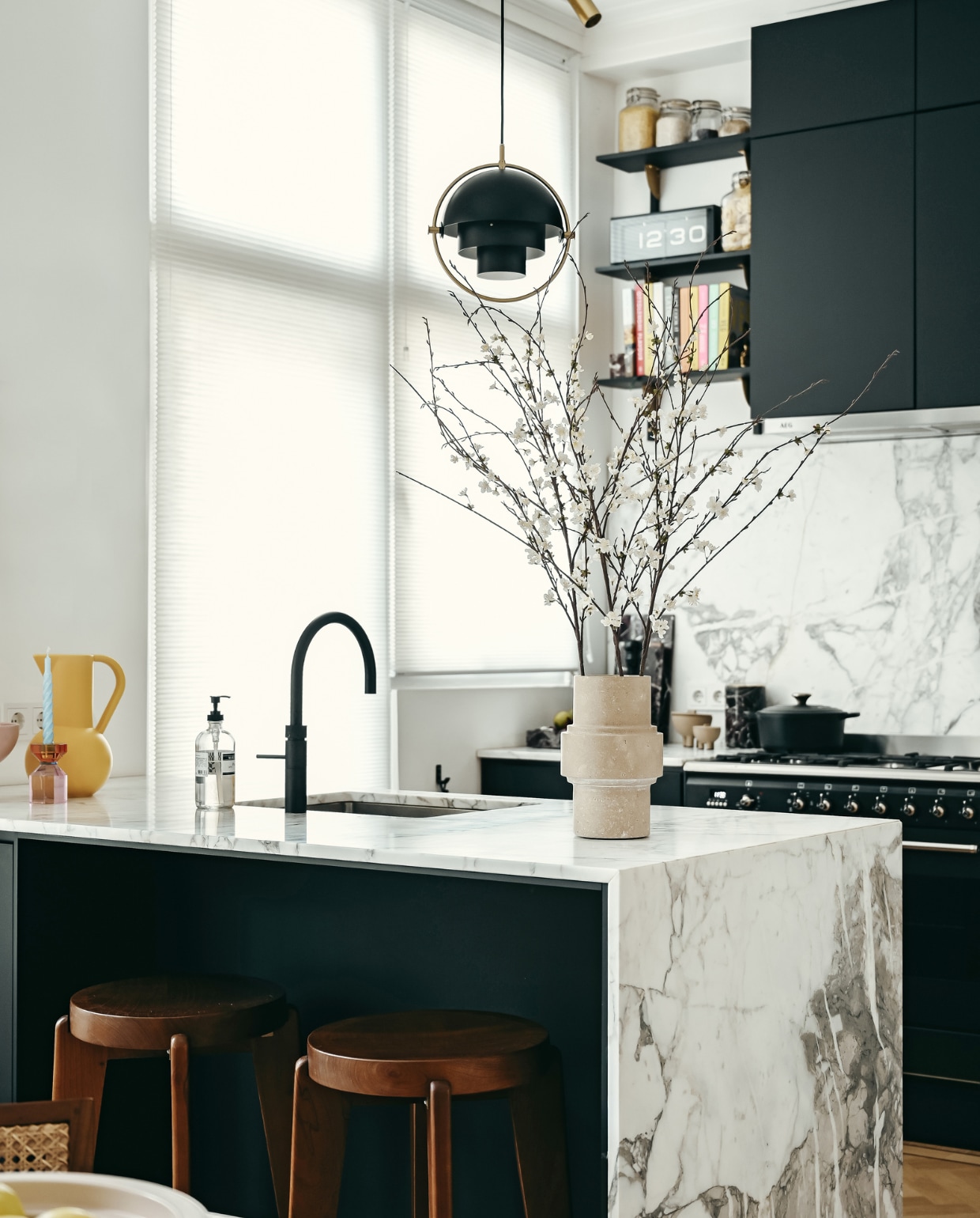 Keukenkasten Kvik, keukenblad en spatwand van Arabscato-marmer Stoned. Kraan Quooker. Barkrukken Detjer. Hanglamp Gubi. Kandelaar Hübsch. Kan raawii. Travertin vaas Column, zwarte, marmeren snijplank en wijnkoeler Stoned. Potjes naast het fornuis 101CPH. vtwonen 01-2023 | styling & fotografie Ellis & Michiel