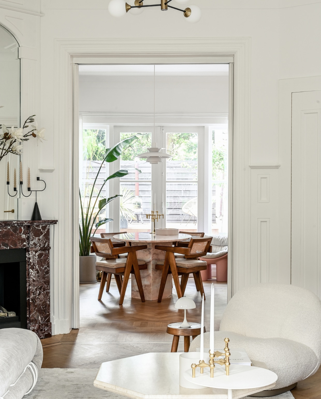 Eettafel en schouw van burgundy-marmer Stoned. Stoelen en houten kruk Detjer. Witte hanglamp PH5 en oplaadbare tafellamp Panthella van Louis Poulsen. Hanglamp met bollen Amazon. Kandelaar op schouw Ferm Living. Fauteuil Gubi. Salontafel vintage. Gouden kandelaar op voorgrond Stoff. Witte bijzettafel &amp;Tradition. Overig onbekend. vtwonen 01-2023 | styling &amp; fotografie Ellis &amp; Michiel