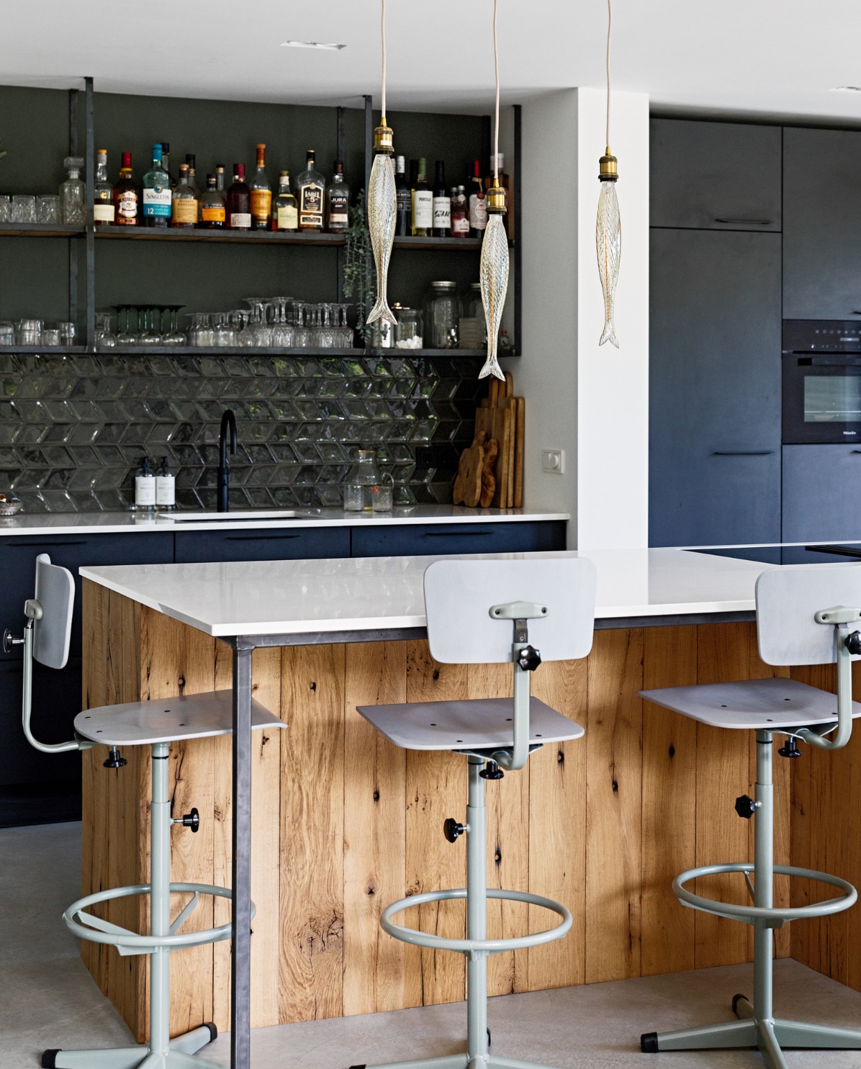 Muurkleur lichte tint Ral 9016, muurkleur donkergroen Ral 7009, vloer gevlinderd beton van Bull beton. Hanglampen vis Bailey via Hollandlamp. Keuken Gebroeders De Wilde, apparatuur Miele, aanrechtblad De Keukenbladenfabriek, hout op de kasten kookeiland oude wagondelen via Frank Pouwer. Stalen hangrek op maat gemaakt Gillissen Ontwerp, whiskyglazen Hutspot, wijnglazen uit Frankrijk, glazen groene voet erfstukken, kleine platte glazen mini amuse glas Bodega. Tegels TGS tegels. Zeepflessen Monday Sunday, tray markt Frankrijk, geurstokjes Wellmark, barstoelen De Machinekamer. vtwonen 12-2022 | styling Ilona Jongepier | fotografie Dana van Leeuwen