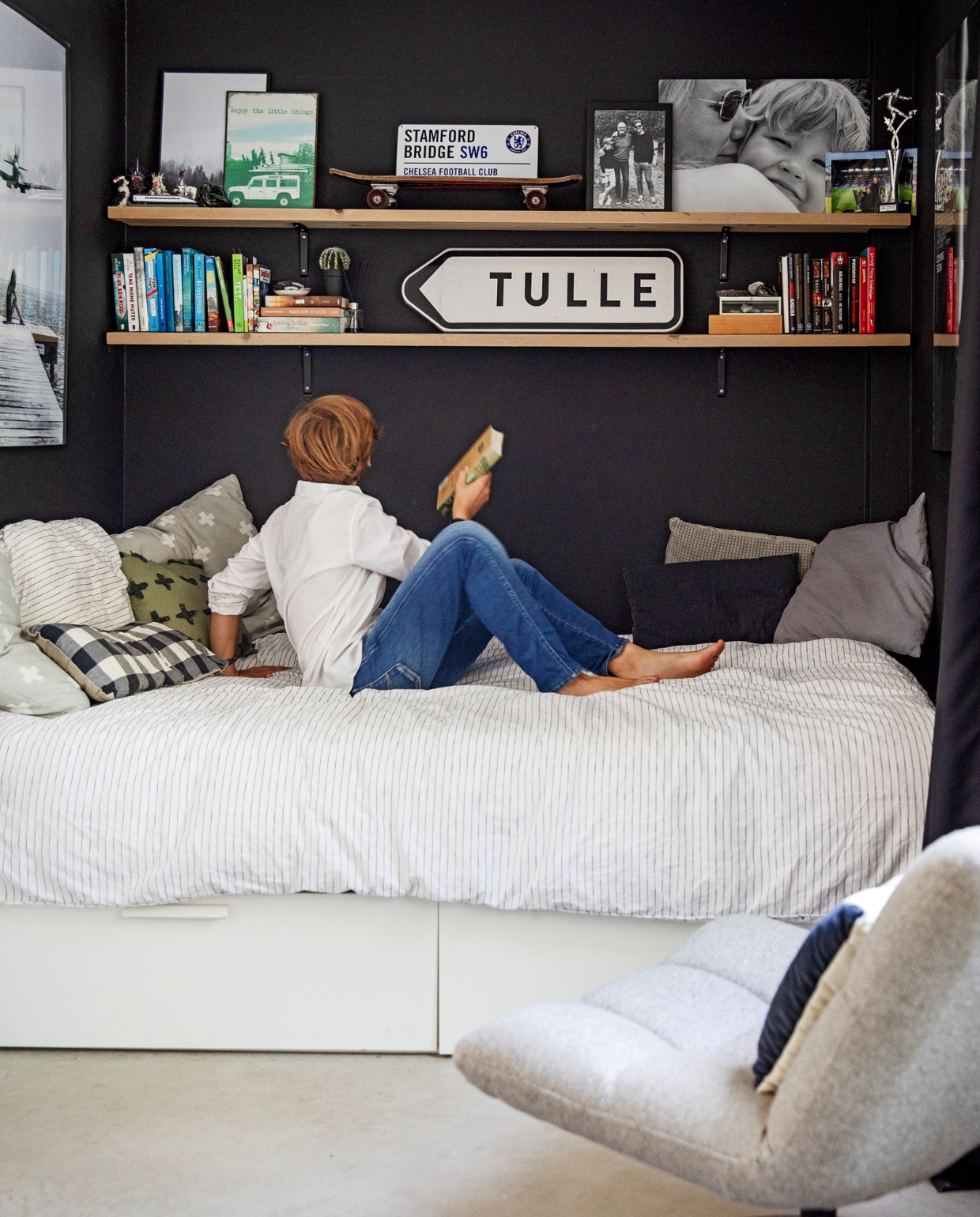 Vloer gevlinderd beton van Bull beton, vloerkleed HKliving. Muurkleur zwart Ral 9005, wandplanken oude steigerplanken Berko. Op de planken: ijzeren borden met afbeeldingen Loods 5, Stanford bridge uit Londen, privéfoto’s, voetbalprijs, verkeersbord Frankrijk. Bed Ikea, beddengoed Vandyck. Kussens (v.l.n.r.) plusjes zelfgemaakt, blokjes Loods 5, groene plusjes Intratuin. Stoel Dutchbone, kussen Deens. vtwonen 12-2022 | styling Ilona Jongepier | fotografie Dana van Leeuwen